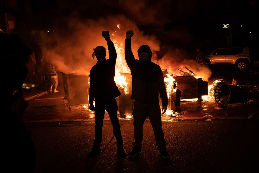 SEATTLE, WA - JUNE 08: Demonstrators raise their fists as a fire burns in the street after clashes with law enforcement near the Seattle Police Departments East Precinct shortly after midnight on June 8, 2020 in Seattle, Washington. Earlier in the evening, a suspect drove into the crowd of protesters and shot one person, which happened after a day of peaceful protests across the city. Later, police and protesters clashed violently during ongoing Black Lives Matter demonstrations following the death of George Floyd. (Photo by David Ryder/Getty Images)