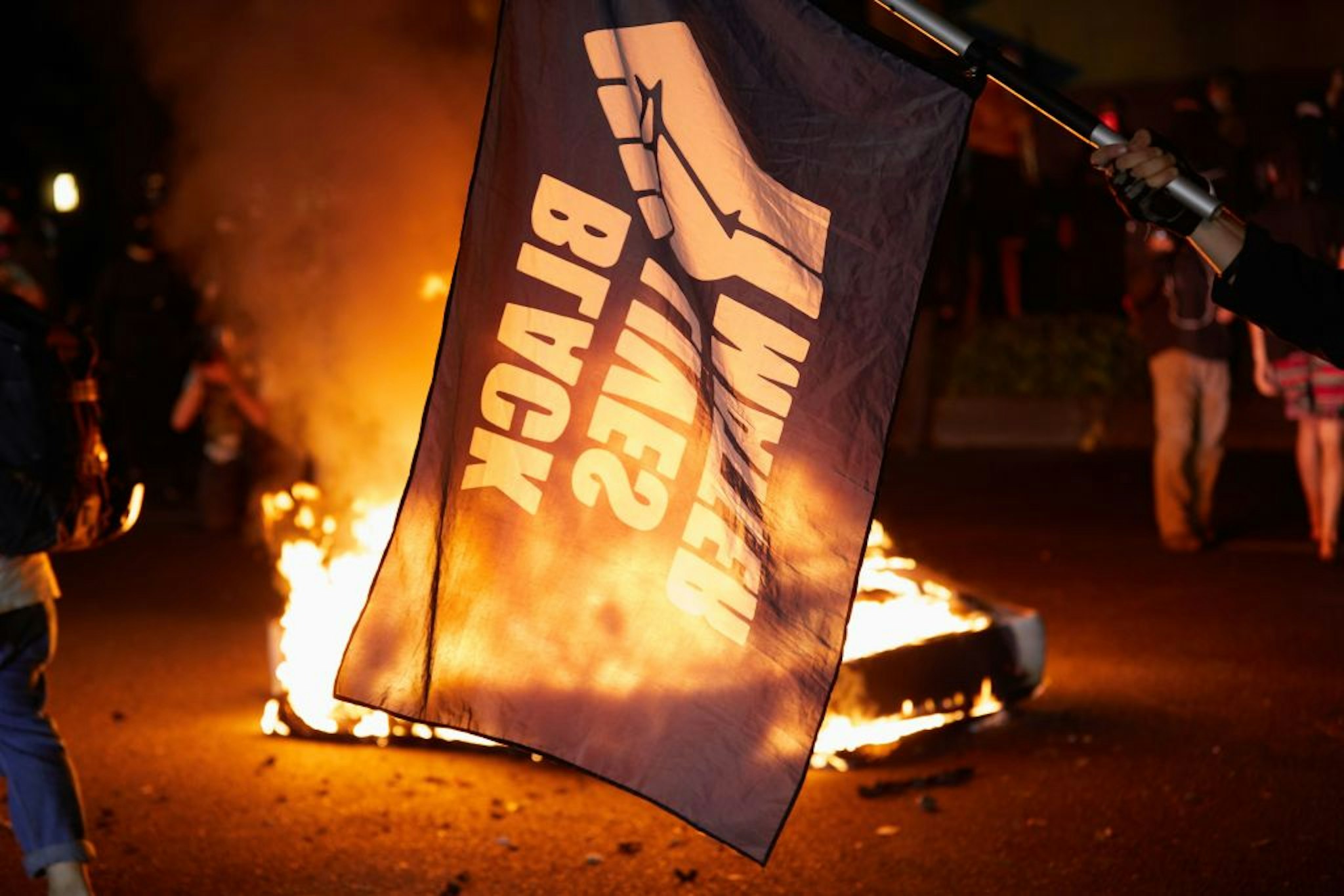 A Black Lives Matter flag waves in front of a fire at the North Precinct Police building in Portland, Oregon on September 6, 2020. - Protestors are marching for an end to racial inequality and police violence. Aaron Danielson, 39, a supporter of a far-right group called Patriot Prayer, was fatally shot August 29, 2020, in Portland, Oregon after he joined pro-Trump supporters who descended on the western US city, sparking confrontations with Black Lives Matter counter-protesters.