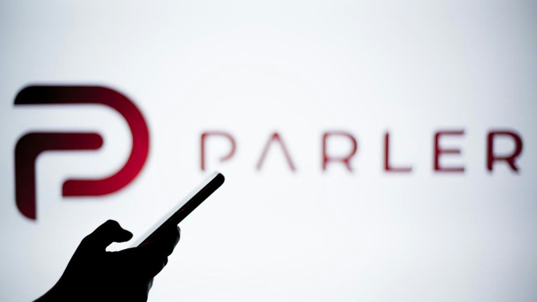 SPAIN - 2021/01/14: In this photo illustration a Parler logo is seen behind a smartphone. The 'free speech' social media platform, Parler, a hit with Trump supporters and an alternative to Twitter, stops working after losing support from Amazon, Apple and Google.