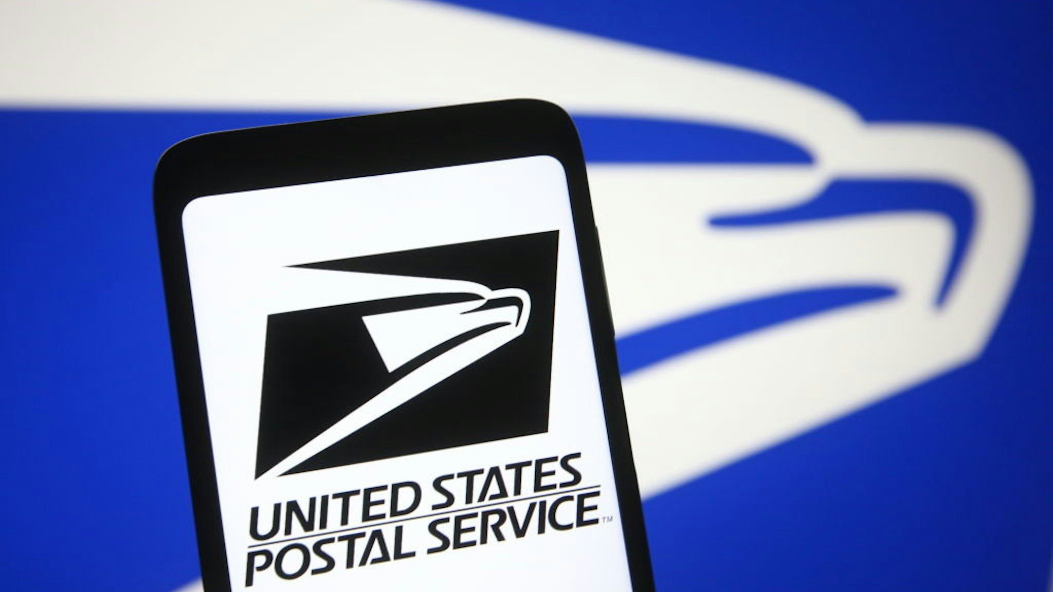In this photo illustration the United States Postal Service (USPS) logo is seen on a smartphone and a pc screen.