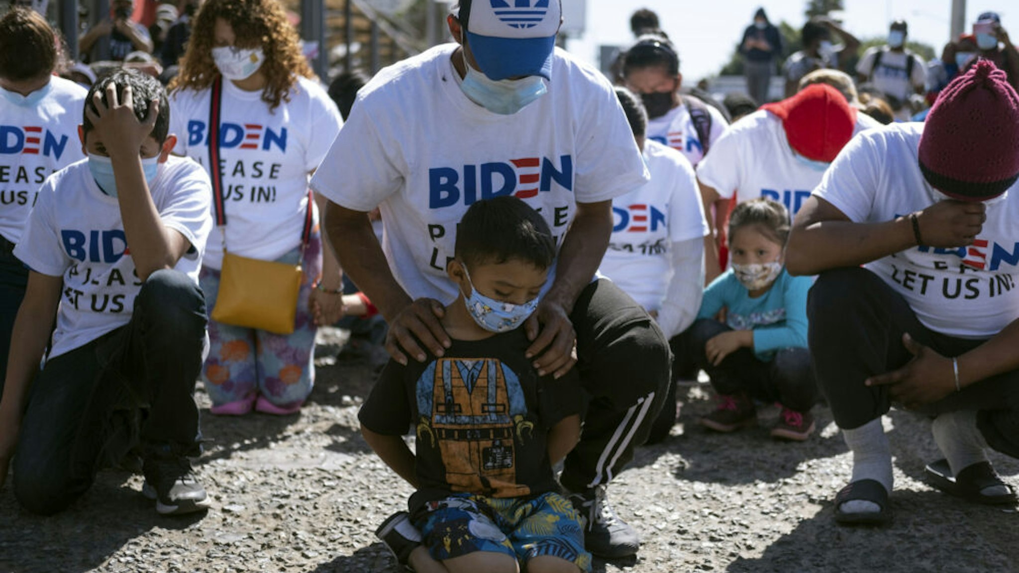 TOPSHOT - Yadiel Garcia and his father Fabricio, from Honduras, kneel as they pray during a migrant demonstration demanding clearer United States migration policies, at San Ysidro crossing port in Tijuana, Baja California state, Mexico on March 2, 2021. - Thousands of migrants out of the Migrant Protection Protocol (MPP) program are stranded along the US-Mexico border without knowing when or how they will be able to start their migratory process with US authorities.