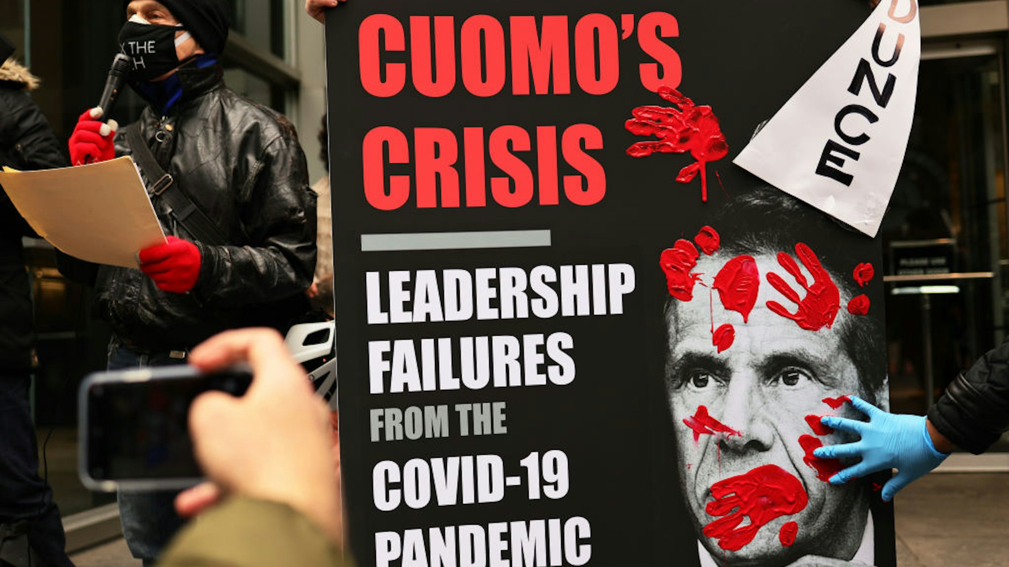 A person places his red painted hands on a poster of Gov. Andrew Cuomo's book as people gather outside of his NYC office to protest against cuts to health care on March 01, 2021 in New York City.