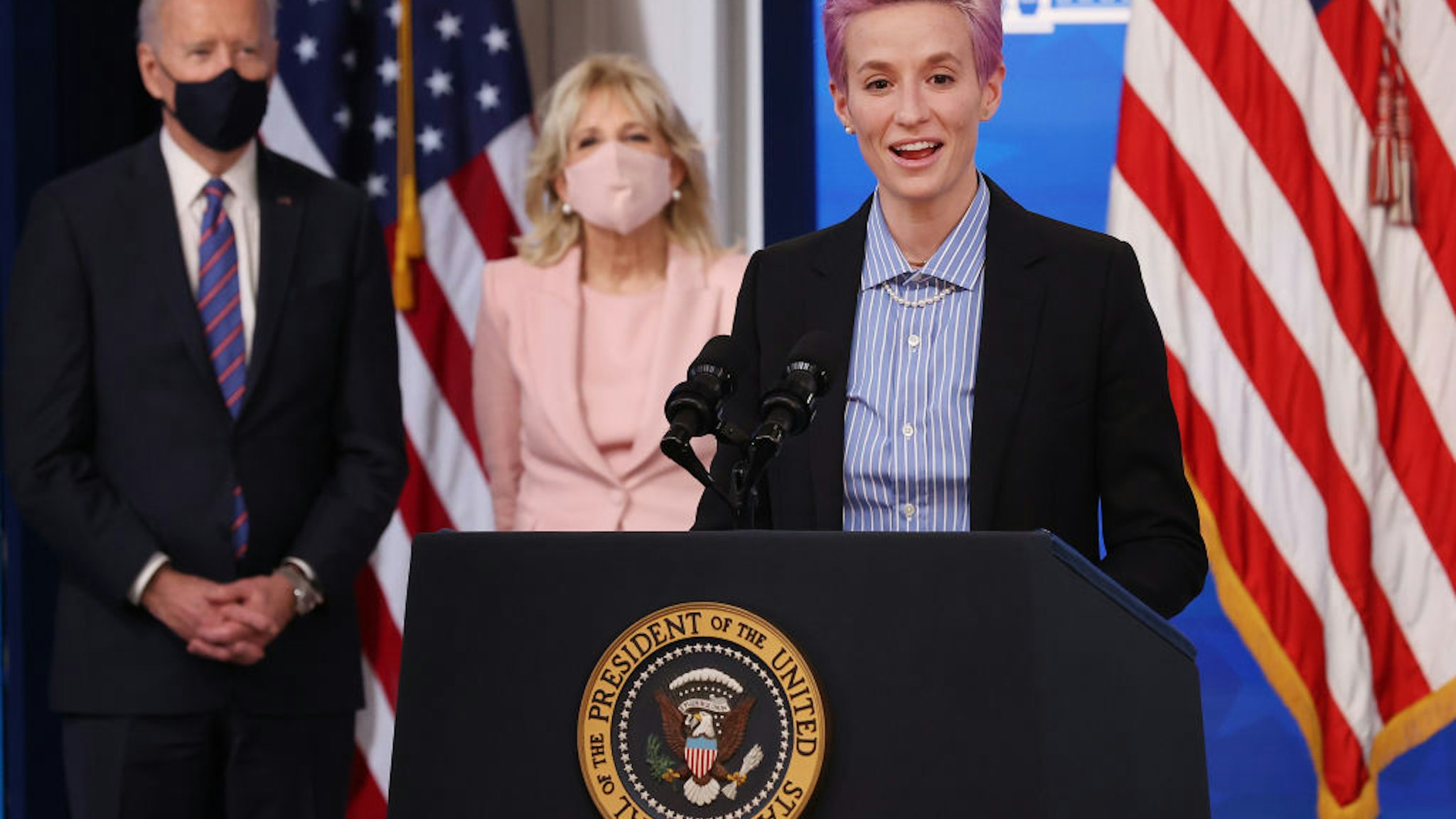 Olympic gold medalist and two-time World Cup champion soccer player Megan Rapinoe deliers remarks during and event to mark Equal Pay Day with U.S. President Joe Biden (L) and first lady Dr. Jill Biden in the South Court Auditorium in the Eisenhower Executive Office Building on March 24, 2021 in Washington, DC.