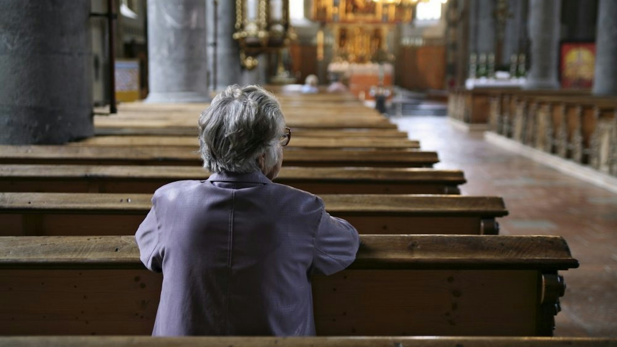 Older woman praying in an almost empty church, rear view