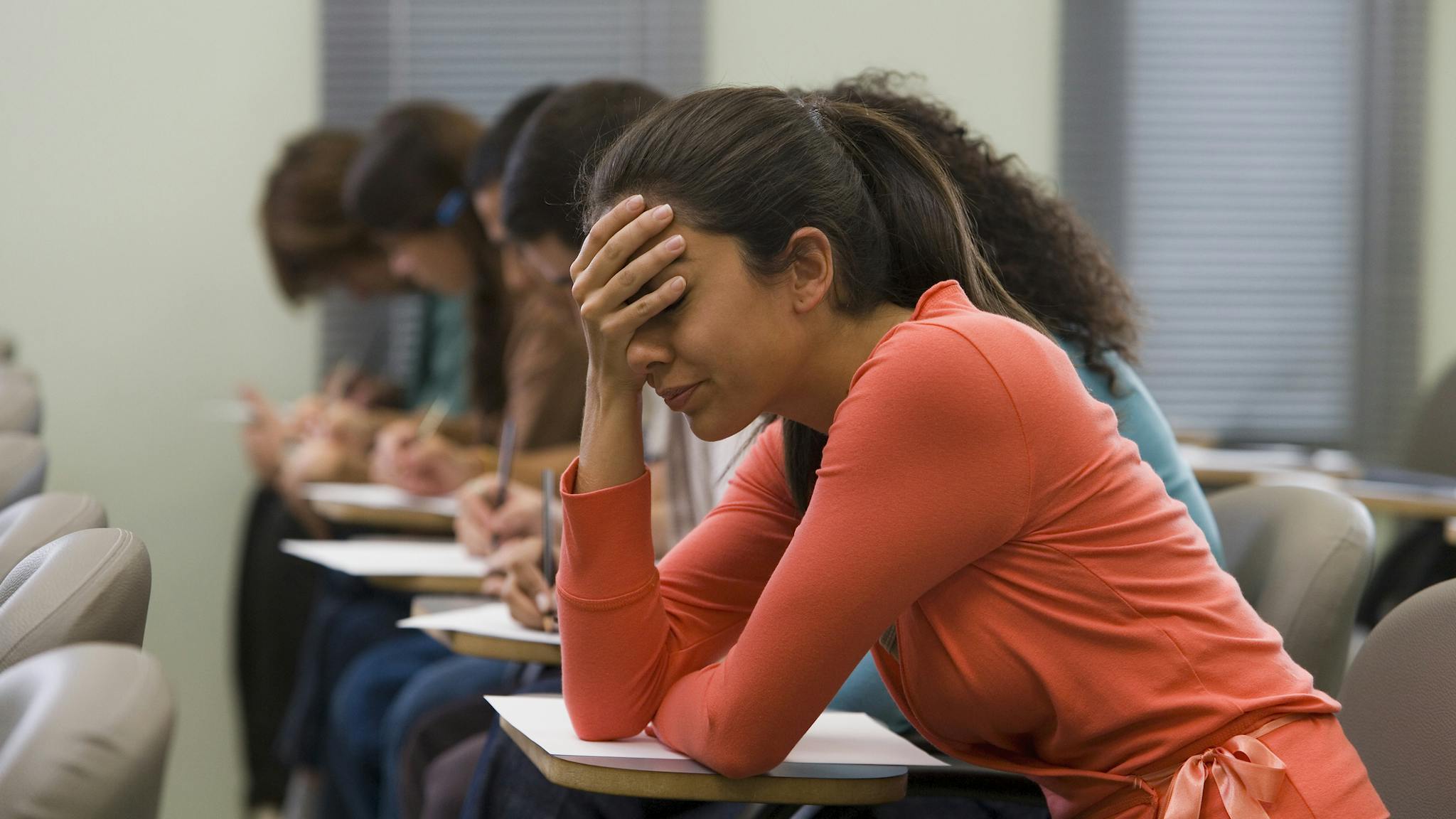 Students taking exam tudents taking written examination, woman holding hand to head - stock photo