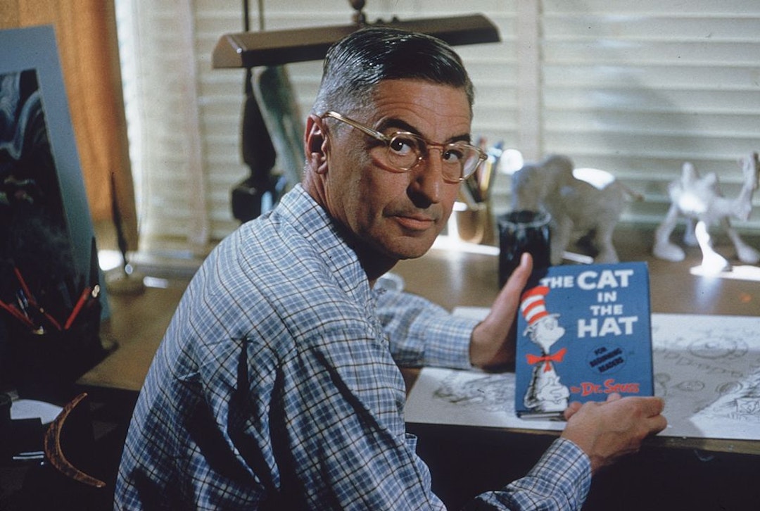 American author and illustrator Dr Seuss (Theodor Seuss Geisel, 1904 - 1991) sits at his drafting table in his home office with a copy of his book, 'The Cat in the Hat', La Jolla, California, April 25, 1957. (Photo by Gene Lester/Getty Images)