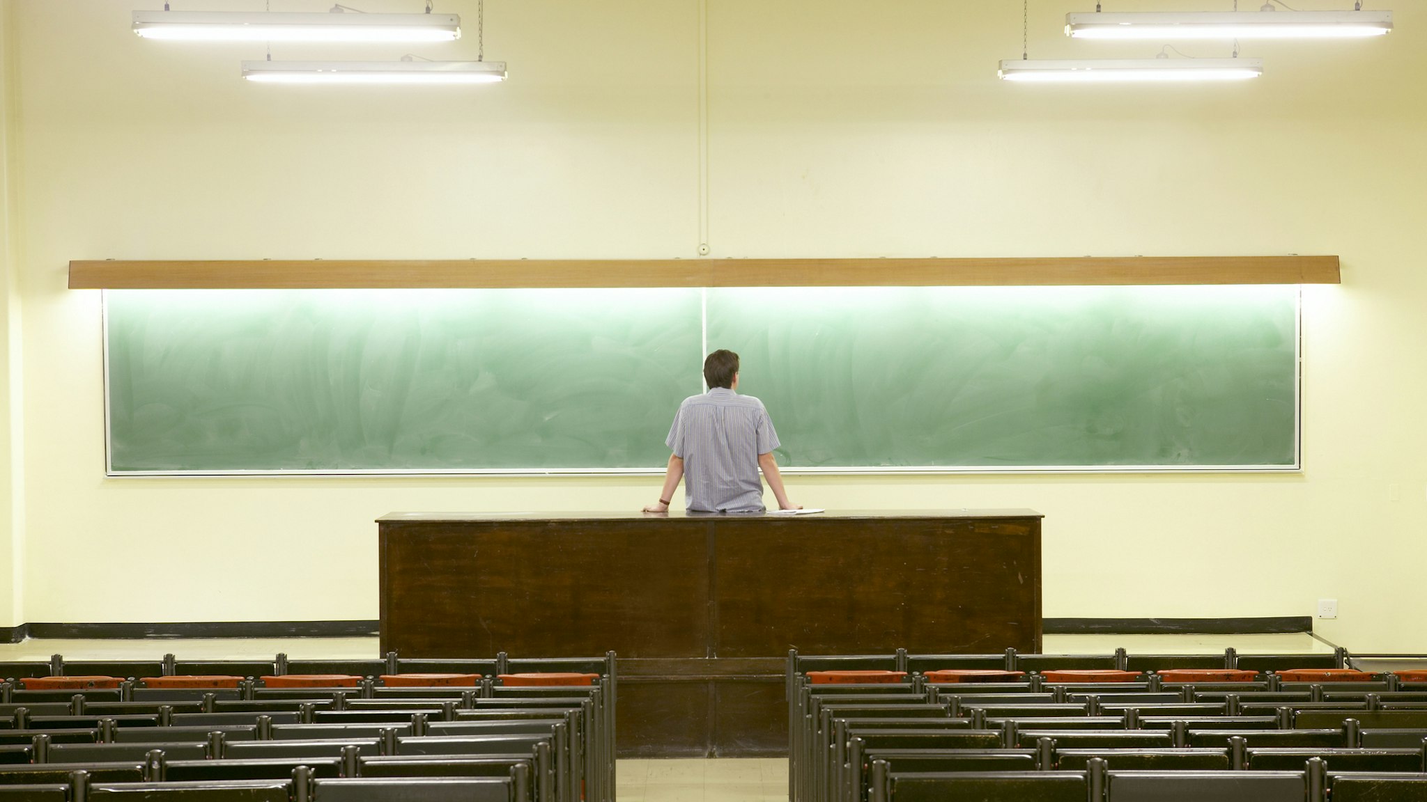 Man Staring at Blackboard in Empty Lecture Hall - stock photo