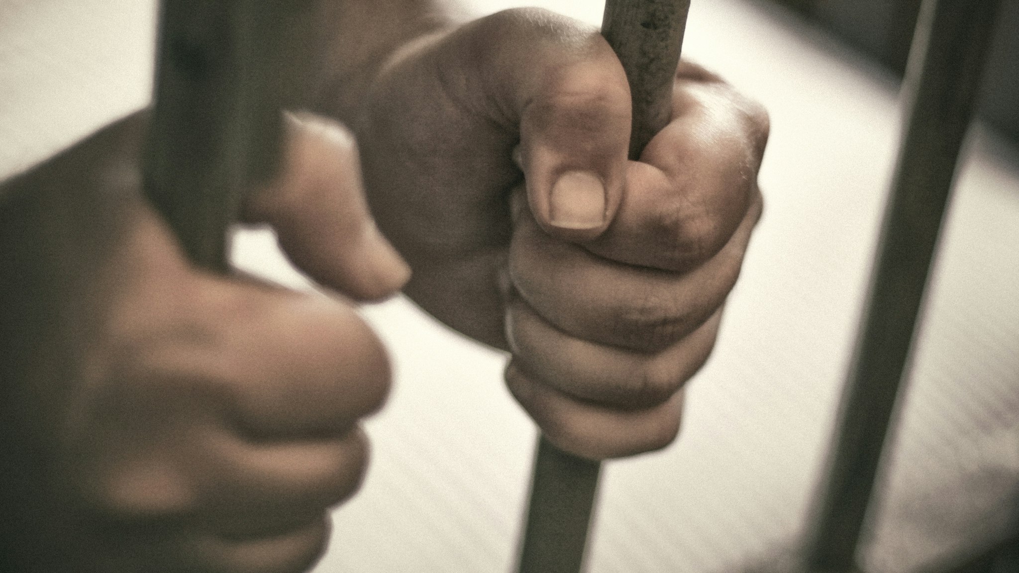 Man's hands tightly holding the bars of his jail cell.