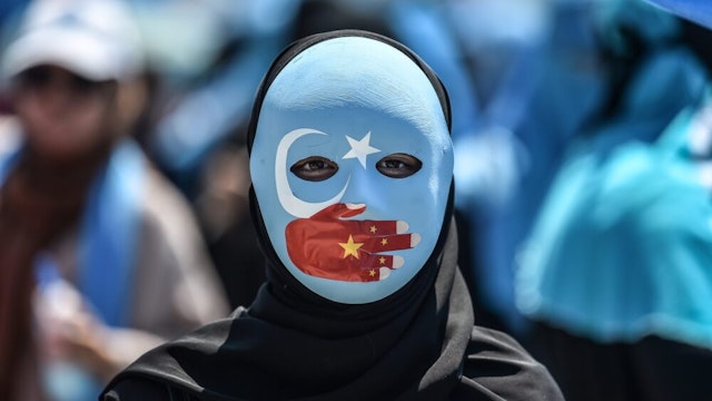 TOPSHOT - A demonstrator wearing a mask painted with the colours of the flag of East Turkestan and a hand bearing the colours of the Chinese flag attends a protest of supporters of the mostly Muslim Uighur minority and Turkish nationalists to denounce China's treatment of ethnic Uighur Muslims during a deadly riot in July 2009 in Urumqi, in front of the Chinese consulate in Istanbul, on July 5, 2018. - Nearly 200 people died during a series of violent riots that broke out on July 5, 2009 over several days in Urumqi, the capital city of the Xinjiang Uyghur Autonomous Region, in northwestern China, between Uyghurs and Han people.
