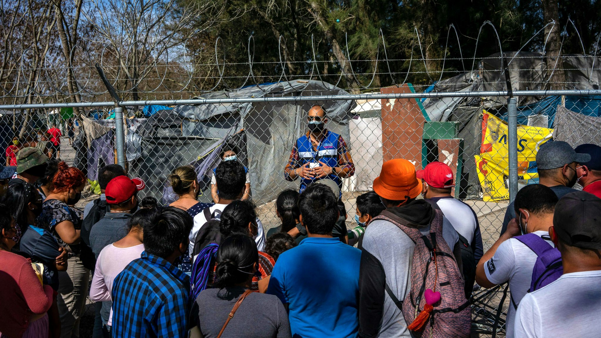 A worker with a nonprofit organization speaks with migrants as they prepare to cross the border into the United States in Matamoros, Tamaulipas state, Mexico, on Friday, Feb. 26, 2021. Emptying the camp in Matamoros would eliminate a symbol of Former U.S. President Donald Trump's immigration crackdown and count as an early success for Presidnt Biden, who aims to undo his predecessor's most draconian anti-immigrant policies.
