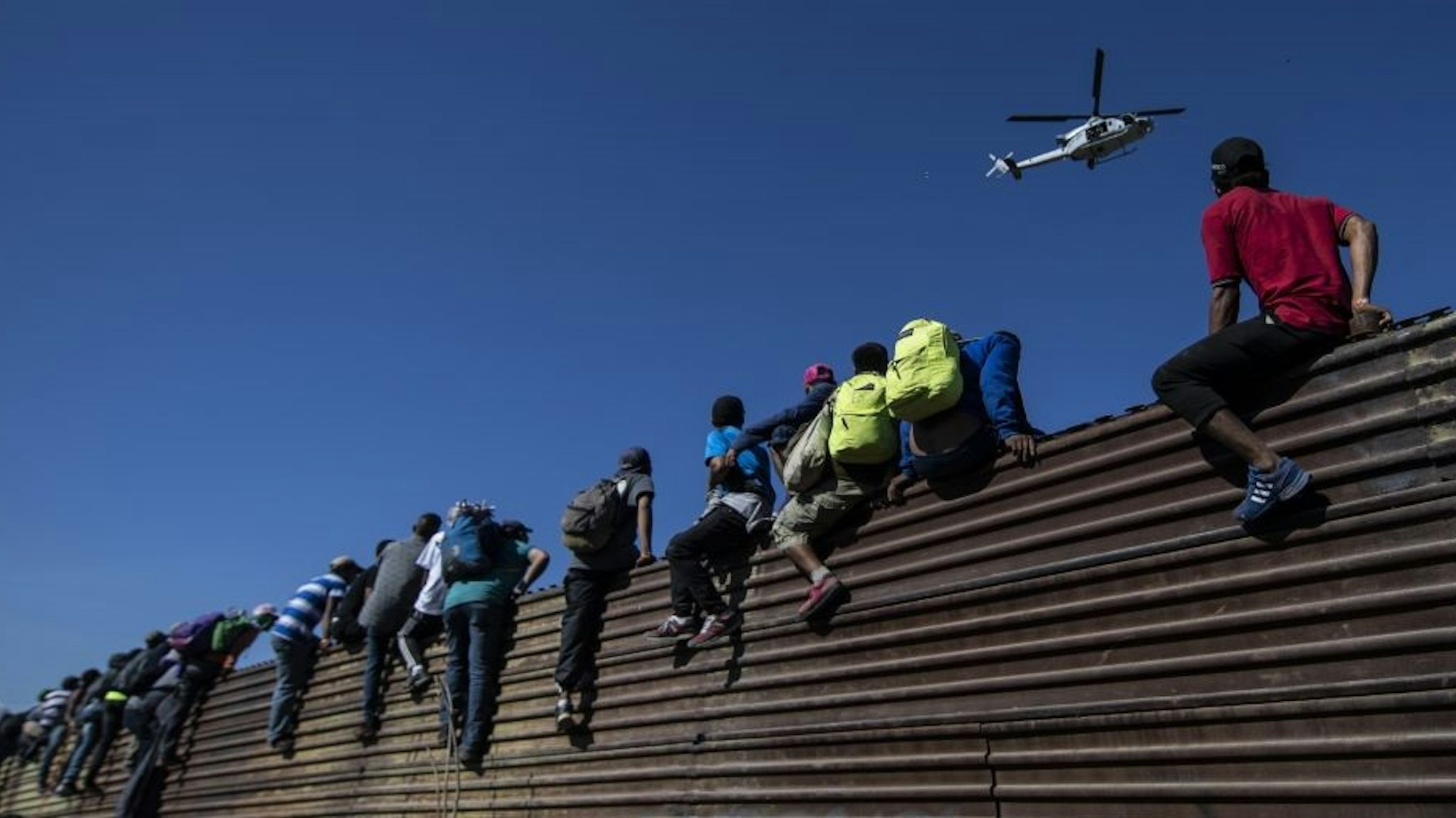 TOPSHOT - A group of Central American migrants -mostly Hondurans- climb a metal barrier on the Mexico-US border near El Chaparral border crossing, in Tijuana, Baja California State, Mexico, on November 25, 2018. - US officials closed the San Ysidro crossing point in southern California on Sunday after hundreds of migrants, part of the "caravan" condemned by President Donald Trump, tried to breach a fence from Tijuana, authorities announced. (Photo by Pedro PARDO / AFP) (Photo credit should read