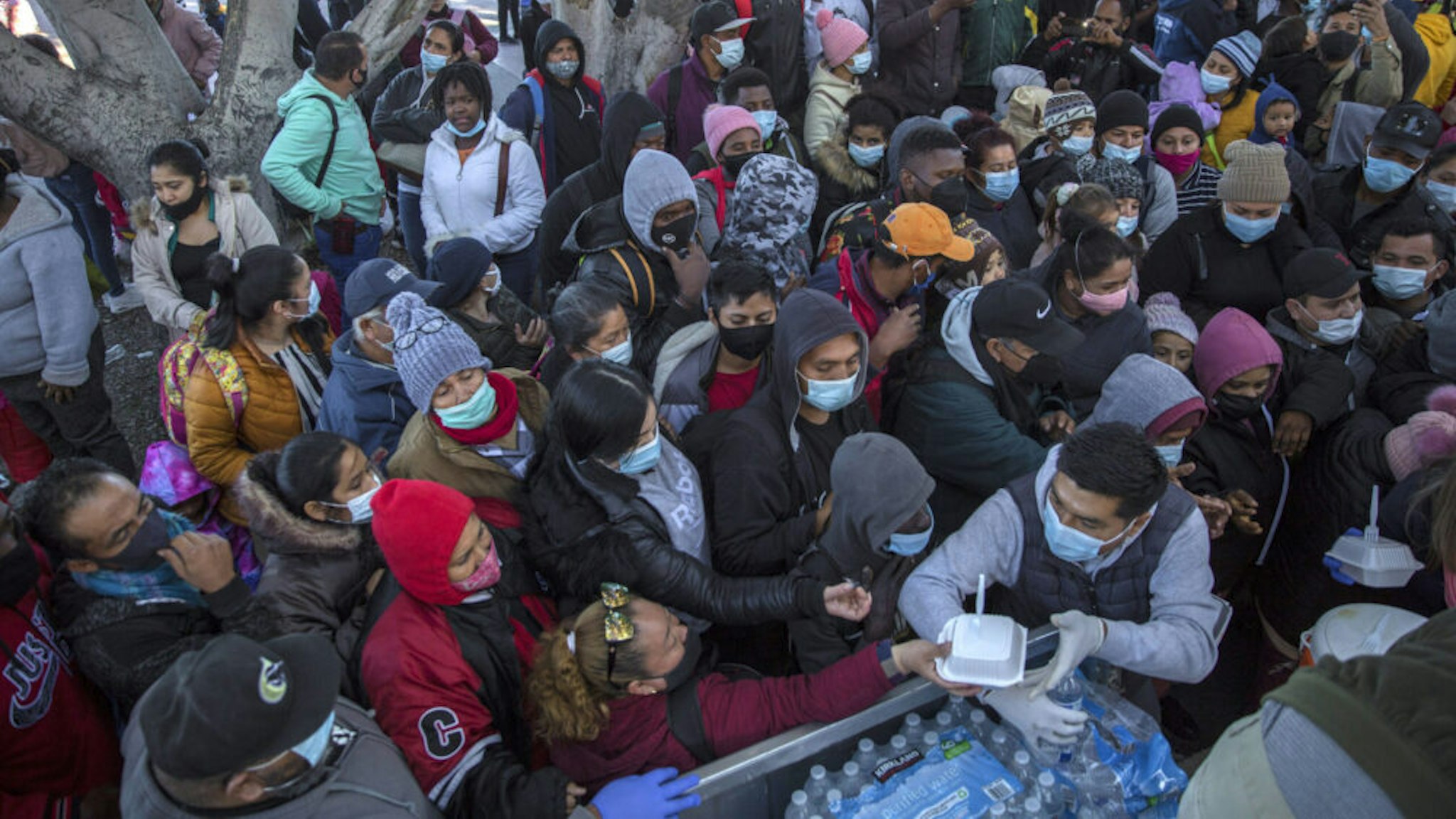 19 February 2021, Mexico, Tijuana: Numerous migrants wearing masks gather and wait for food and water to be distributed at the border crossing. Following the announced change of direction in US migration policy, numerous migrants have gathered at the border between Mexico and the US, hoping to gain entry to the US. With the new regulation US President Biden's administration is breaking with the restrictive immigration policy of his predecessor Trump.