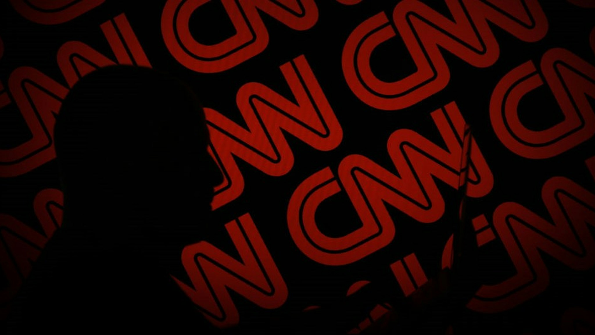A man is seen holding with a smart device in front of a CNN logo in this photo illustration on 2 July, 2017. (Photo by