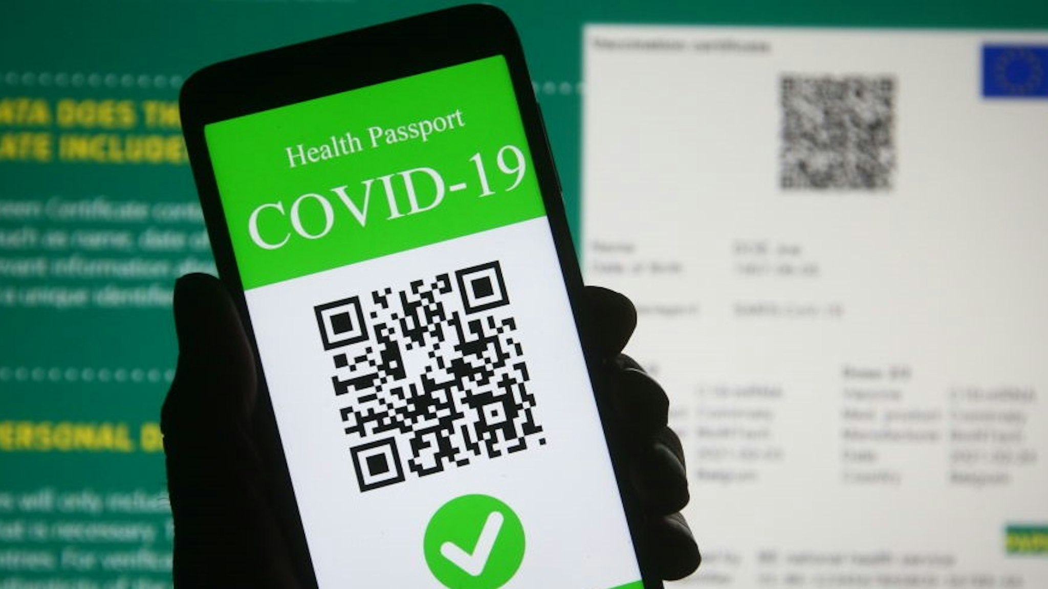 UKRAINE - 2021/03/28: In this photo illustration, a symbolic COVID-19 health passport seen displayed on a smartphone screen in front of the European Commission information about a proposal to create a Digital Green Certificate. On March 17 the European Commission presented a proposal to create a Digital Green Certificate to facilitate the safe free movement of the EU citizens during the COVID-19 pandemic. (Photo Illustration by