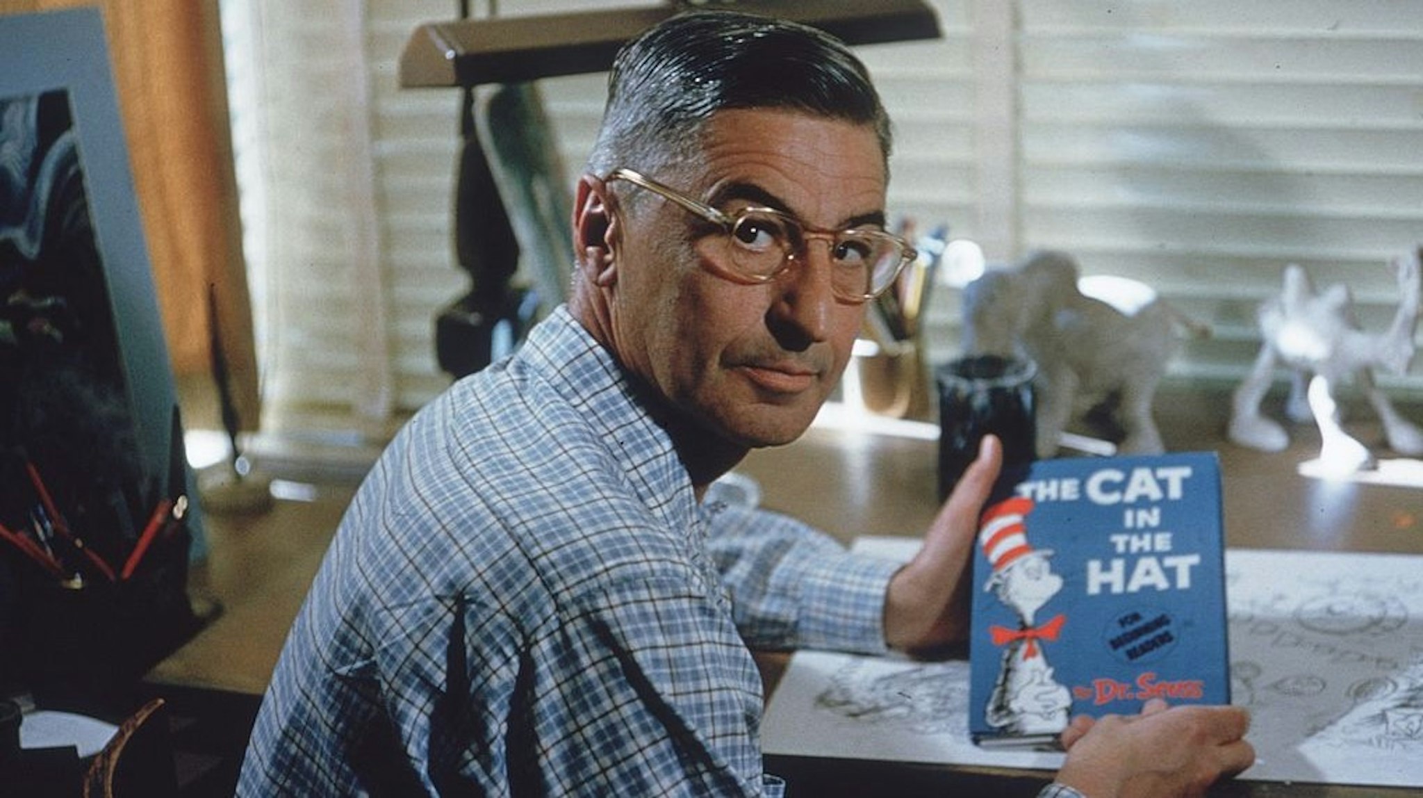 American author and illustrator Dr Seuss (Theodor Seuss Geisel, 1904 - 1991) sits at his drafting table in his home office with a copy of his book, 'The Cat in the Hat', La Jolla, California, April 25, 1957. (Photo by