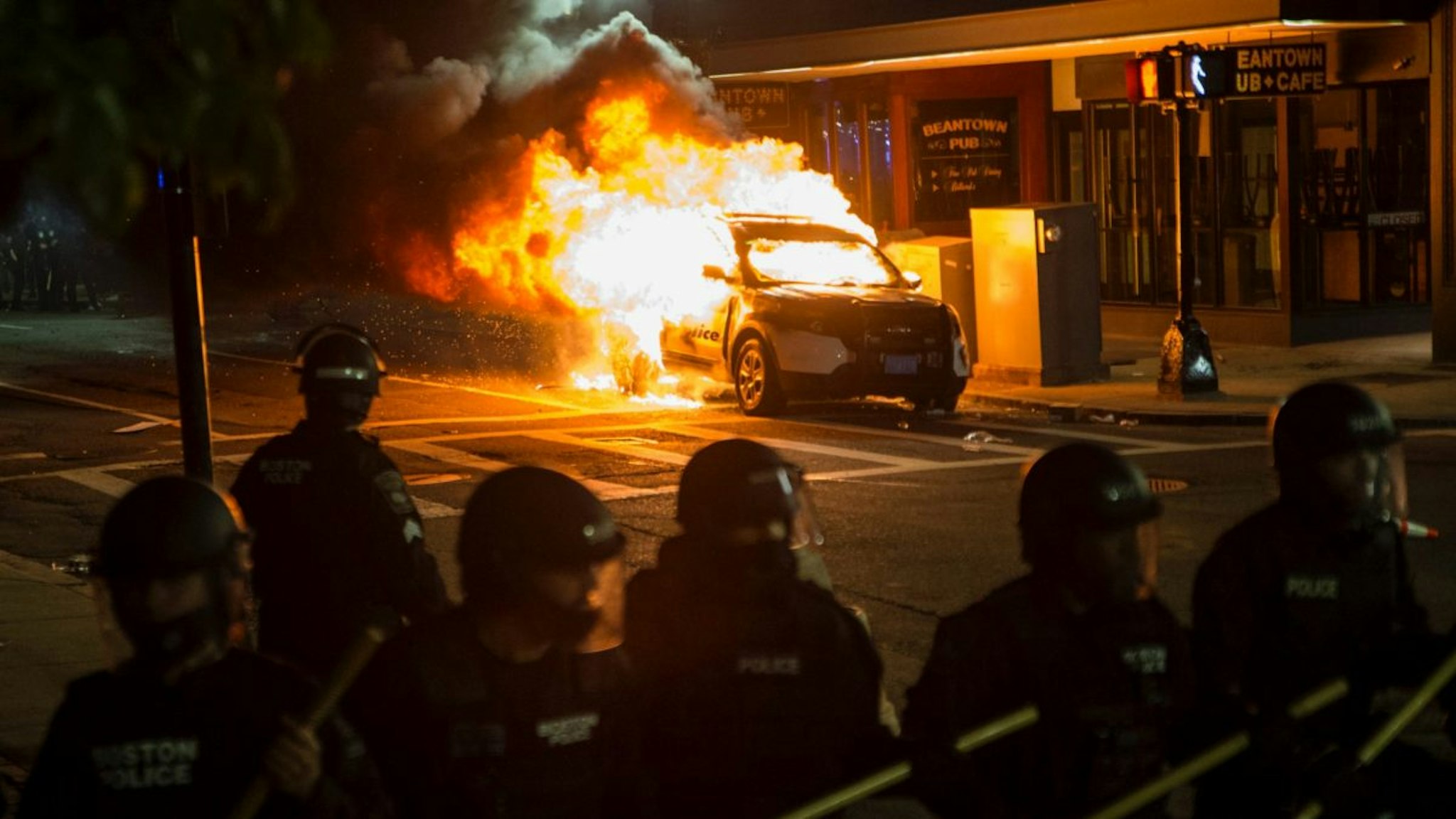 A police cruiser burns behind the Police line near the intersection of Park and Tremont as a protest against police brutality pushes through the streets of Boston on May 31, 2020.