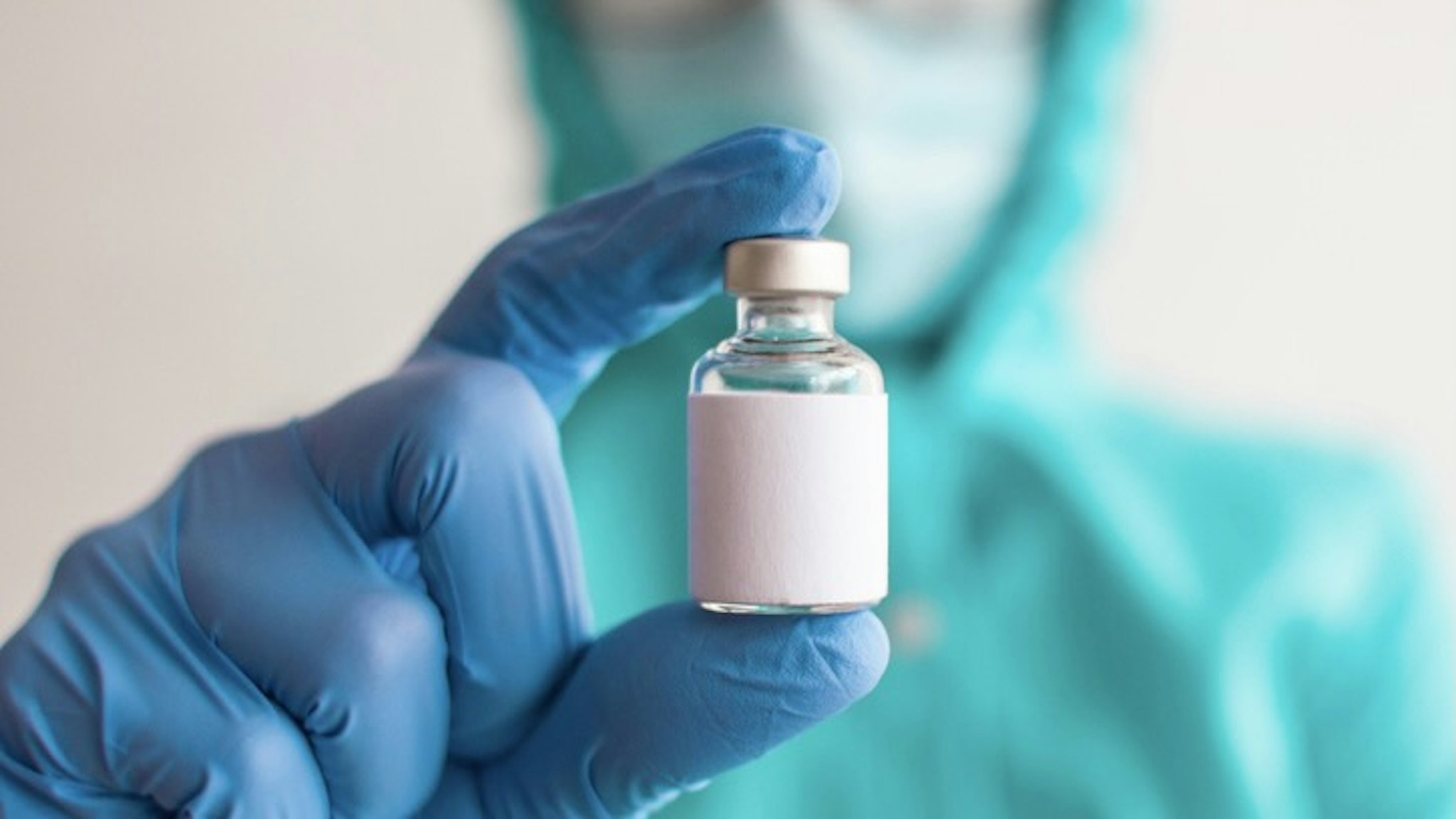 A female healthcare worker is holding a medicine vial - stock photo A female healthcare worker in vibrant colored protective suit is holding a medicine vial