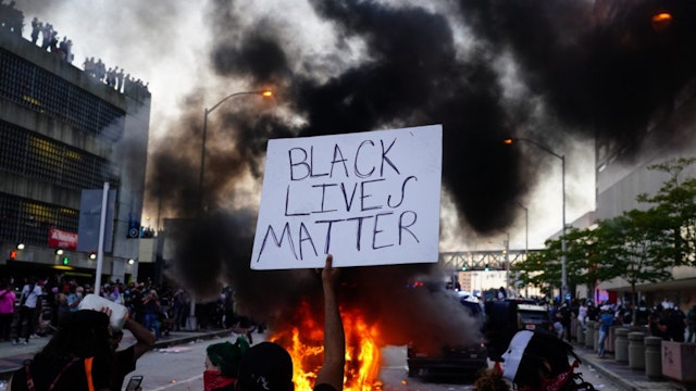 29: A man holds a Black Lives Matter sign as a police car burns during a protest on May 29, 2020 in Atlanta, Georgia.
