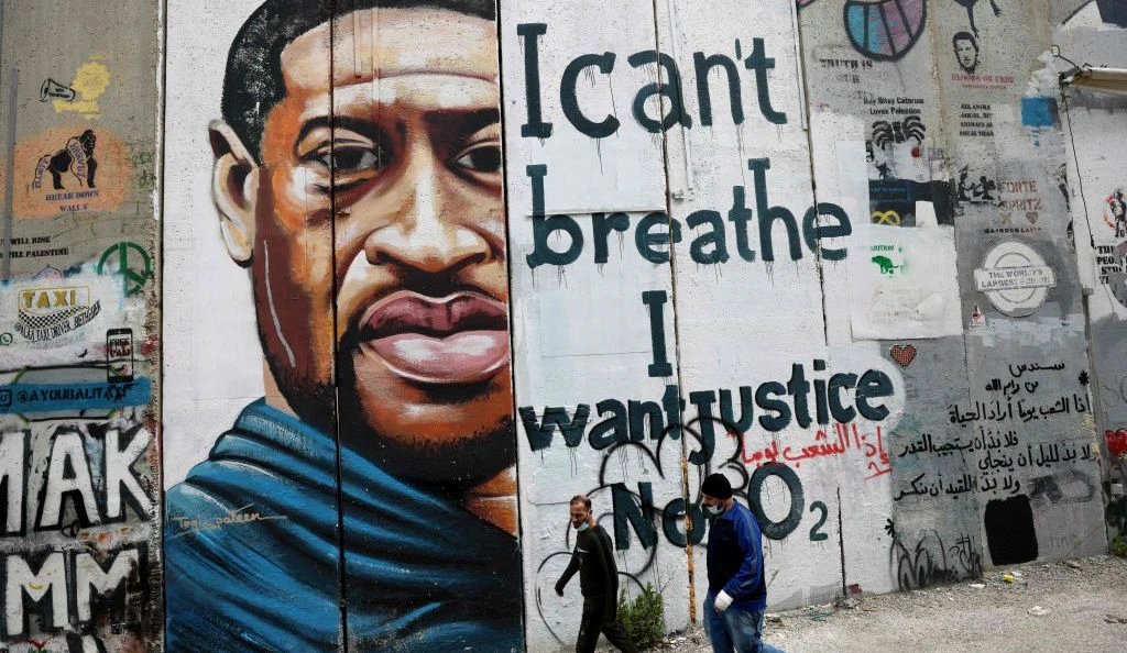 People walk past a mural showing the face of George Floyd, an unarmed handcuffed black man who died after a white policeman knelt on his neck during an arrest in the US, painted on a section of Israel's controversial separation barrier in the city of Bethlehem in the occupied West Bank on March 31, 2021. (Photo by EMMANUEL DUNAND/AFP via Getty Images)