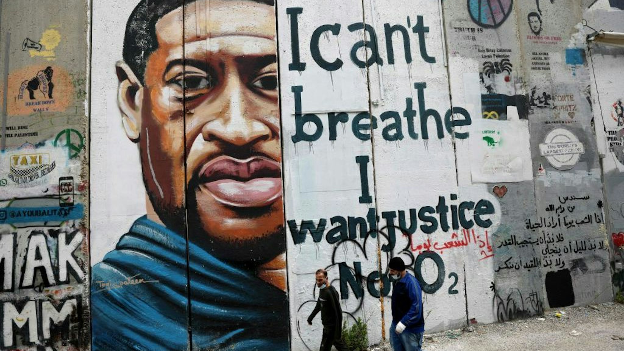 People walk past a mural showing the face of George Floyd, an unarmed handcuffed black man who died after a white policeman knelt on his neck during an arrest in the US, painted on a section of Israel's controversial separation barrier in the city of Bethlehem in the occupied West Bank on March 31, 2021. (Photo by EMMANUEL DUNAND/AFP via Getty Images)