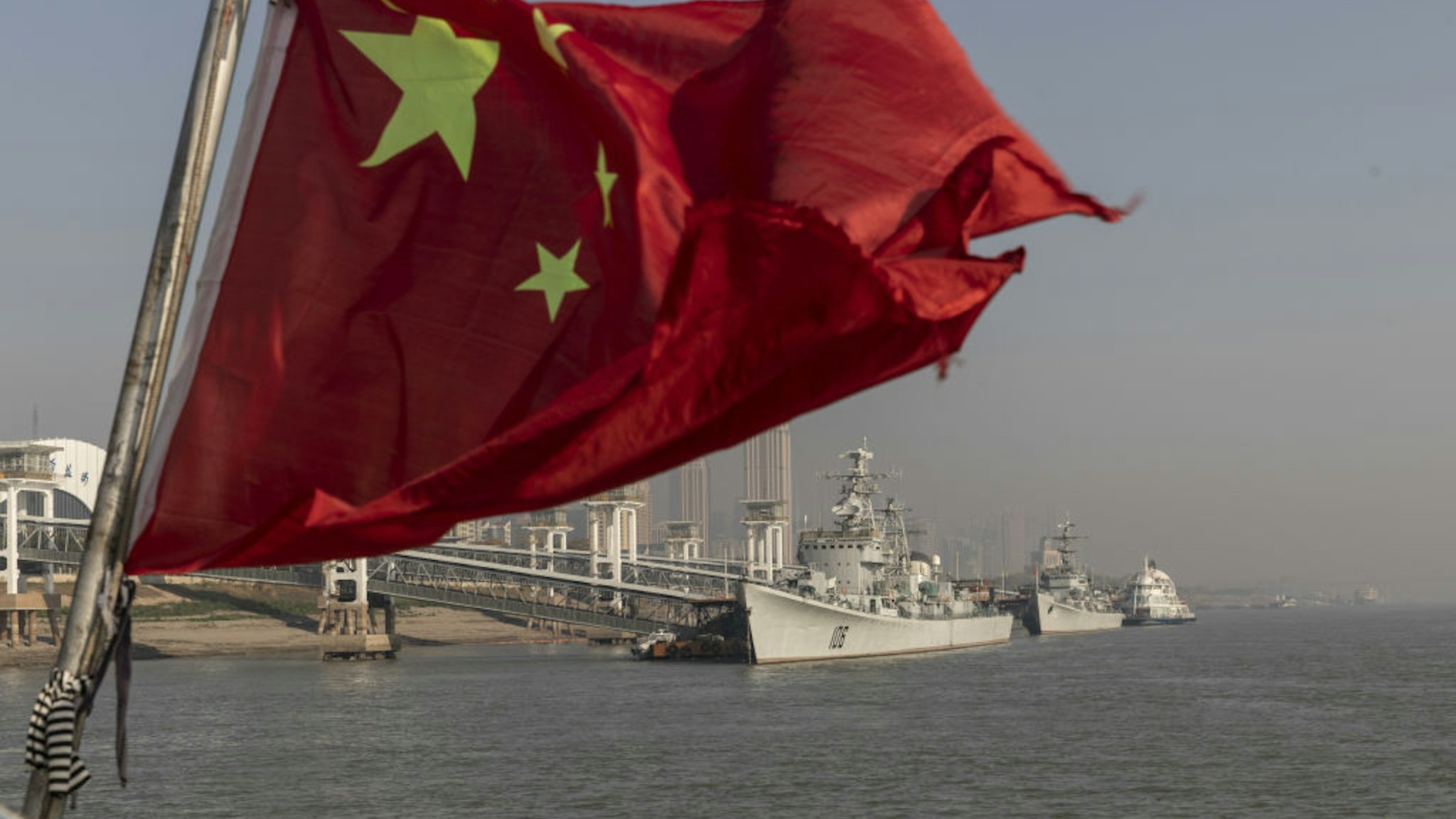 A Chinese national flag flies from a ferry as the retired People's Liberation Army (PLA) Navy Xian frigate ship, from left, and the Huaian frigate ship sit anchored on the Yangtze River in Wuhan, Hubei, China, on Wednesday, Dec. 11, 2019. China's economic growth will come in at 5.9% in 2020 as easing trade tensions and the prospect of lower bank borrowing costs boost confidence, according to analysts and traders.