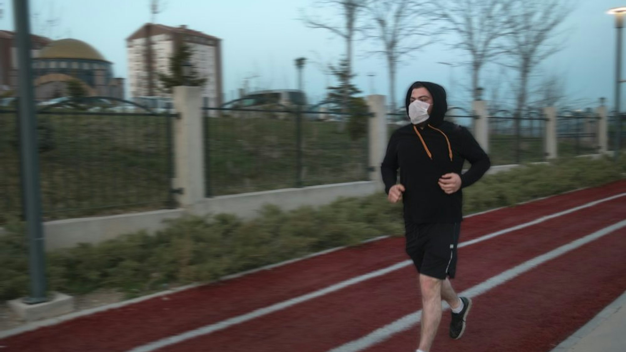 Isolated young man wearing mask and a hoodie running at a parkIsolated young man wearing mask and a hoodie running at a park