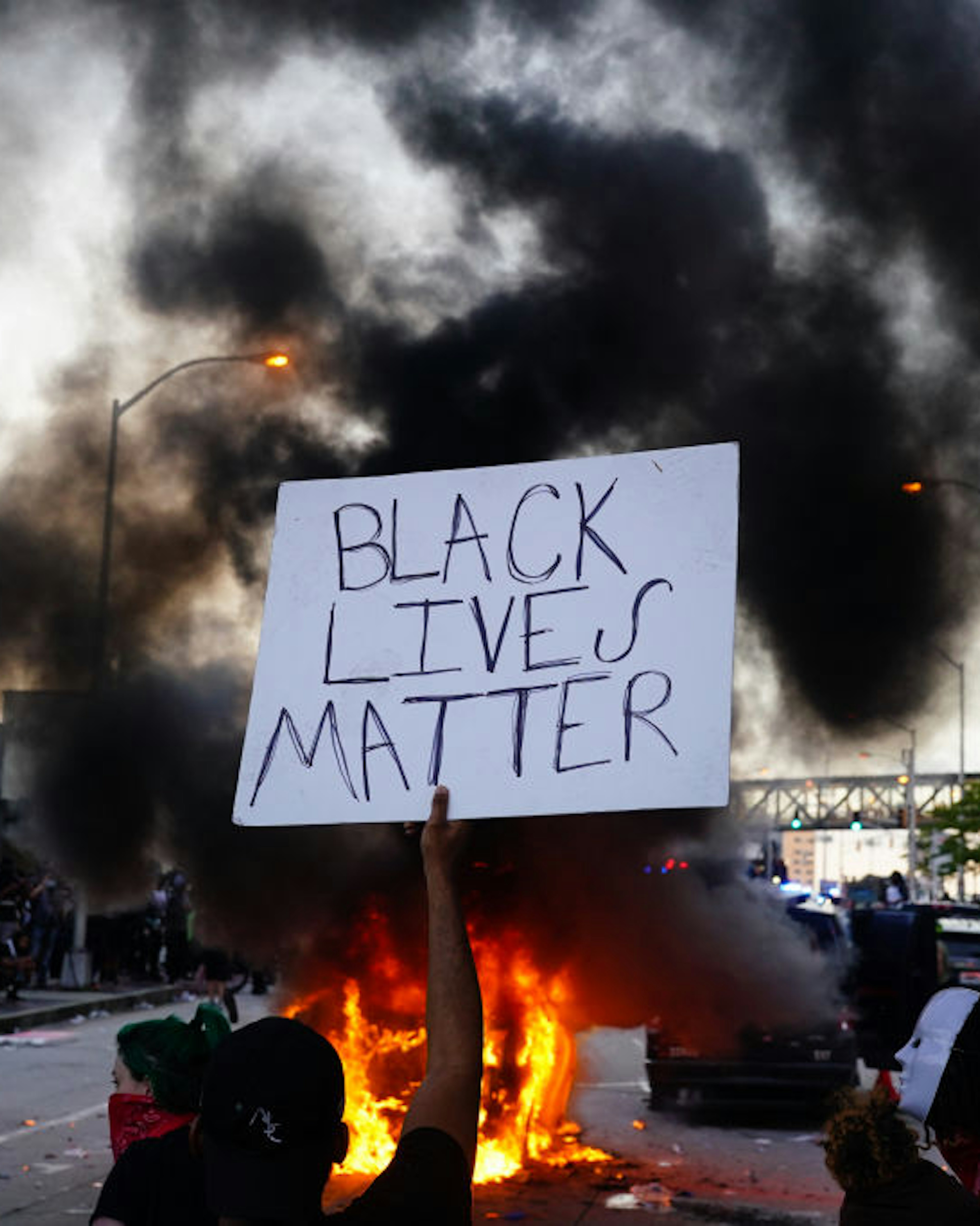 ATLANTA, GA - MAY 29: A man holds a Black Lives Matter sign as a police car burns during a protest on May 29, 2020 in Atlanta, Georgia. Demonstrations are being held across the US after George Floyd died in police custody on May 25th in Minneapolis, Minnesota. (Photo by Elijah Nouvelage/Getty Images)