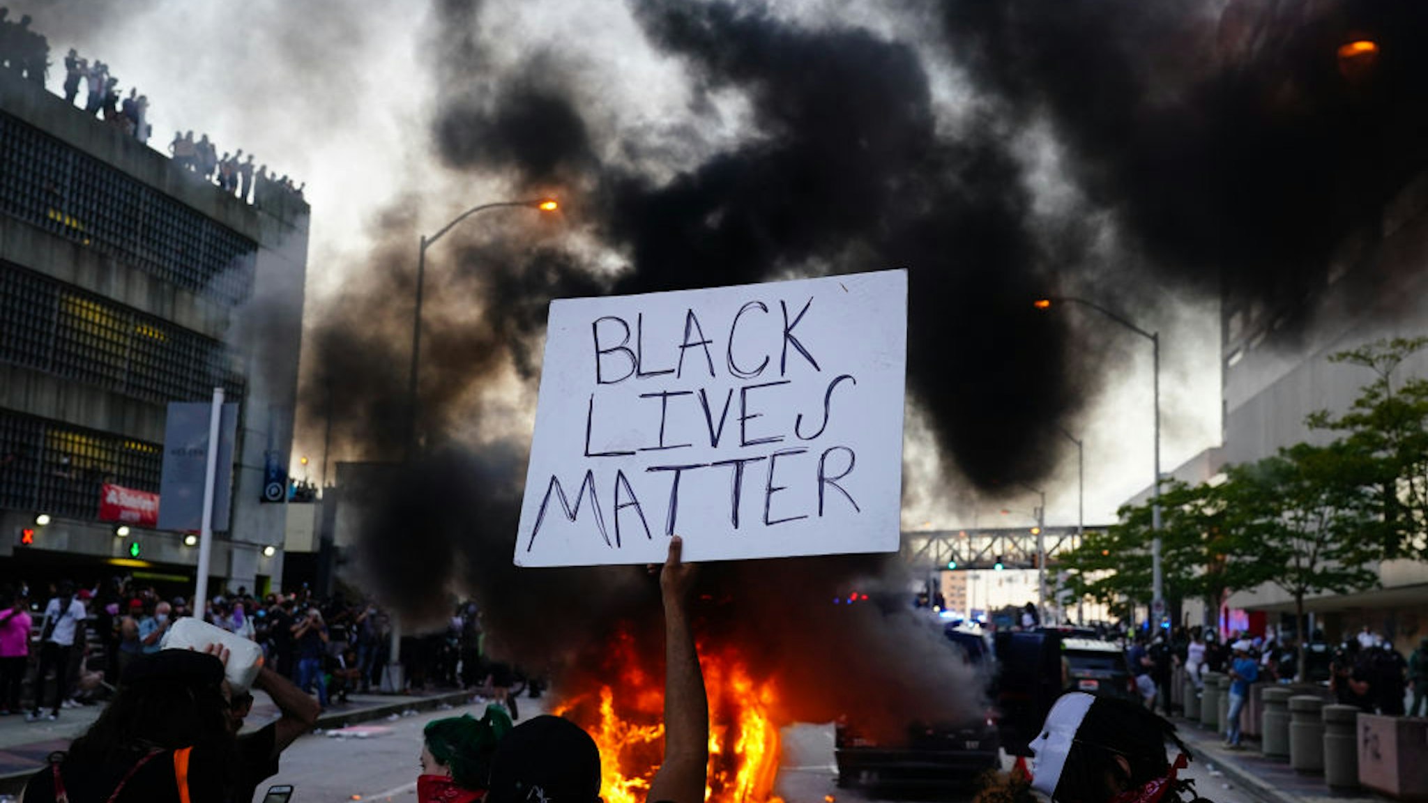 ATLANTA, GA - MAY 29: A man holds a Black Lives Matter sign as a police car burns during a protest on May 29, 2020 in Atlanta, Georgia. Demonstrations are being held across the US after George Floyd died in police custody on May 25th in Minneapolis, Minnesota.