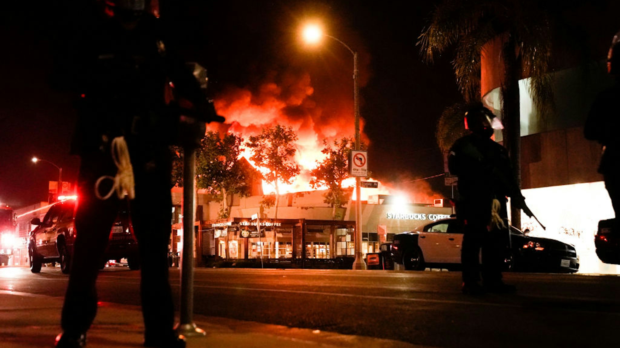 Law enforcement officers with a structure ablaze int he background in the Fairfax District on Saturday, May 30, 2020 in Los Angeles, CA.