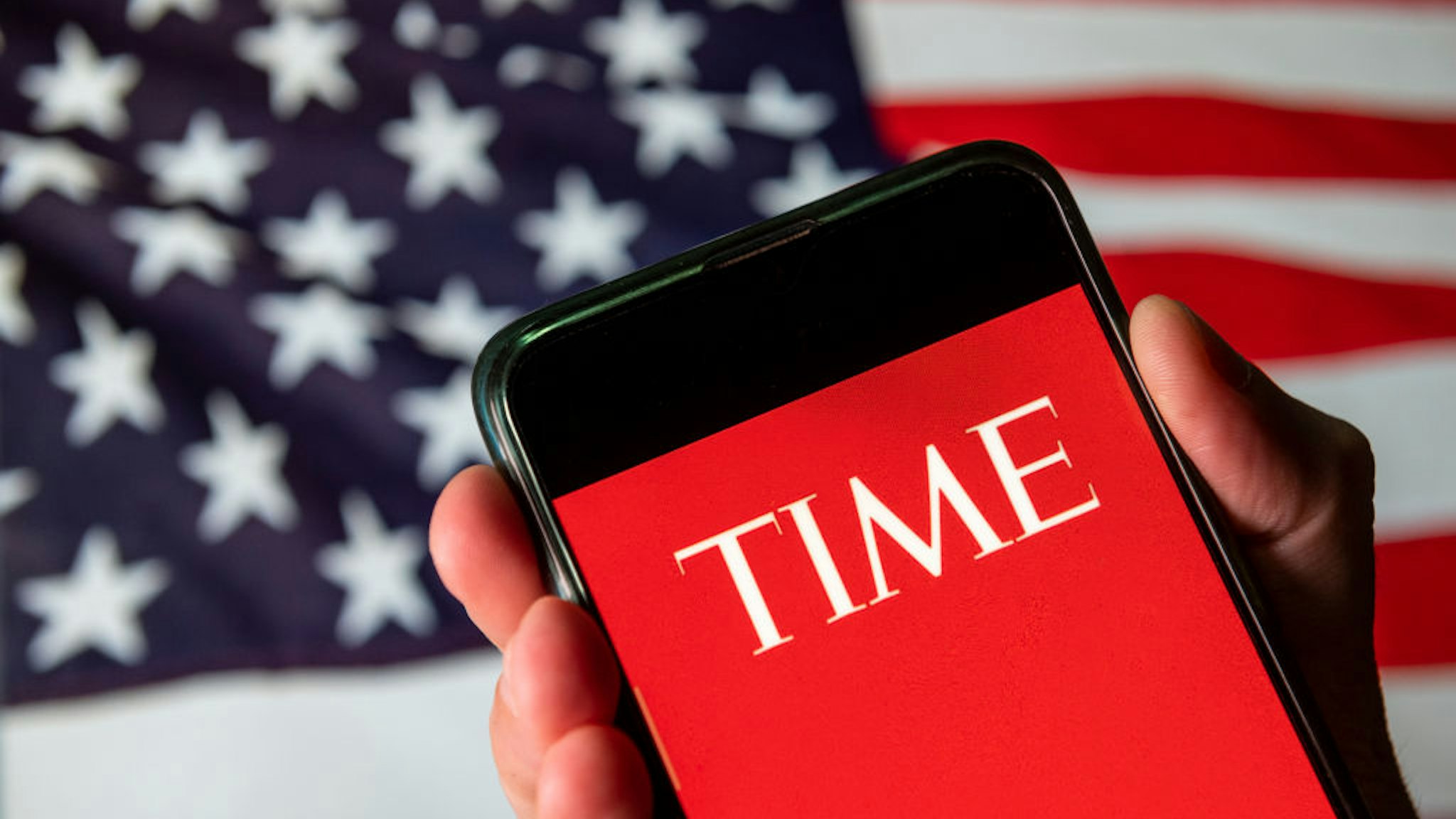 CHINA - 2020/08/13: In this photo illustration the American weekly news magazine and news website Time logo is seen on an Android mobile device with United States of America flag in the background.