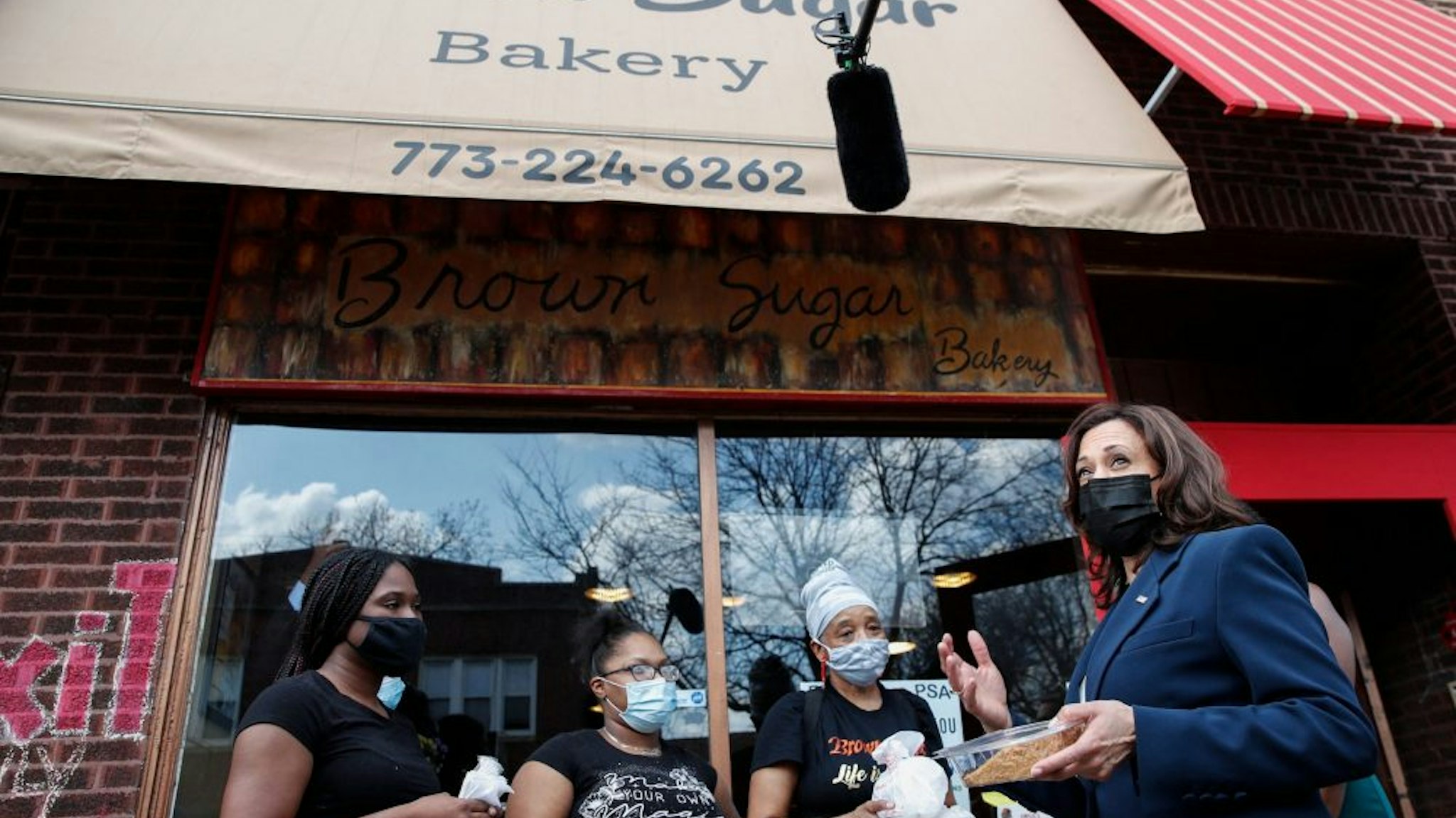US Vice President Kamala Harris (R) chats with workers as she receives a piece of German Chocolate Cake outside of the Brown Sugar Bakery during a quick stop in Chicago, Illinois, on April 6, 2021. - Harris toured earlier in the day a Covid-19 vaccination site, a partnership between the city of Chicago and the Chicago Federation of Labor.