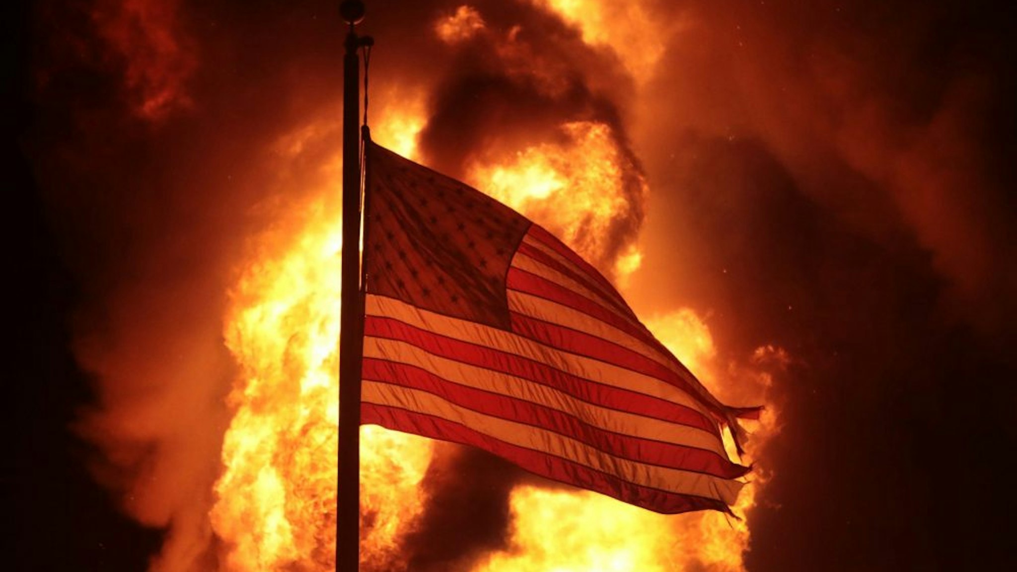 KENOSHA, WISCONSIN - AUGUST 24: A flag flies in front of a department of corrections building after it was set ablaze during a second night of rioting on August 24, 2020 in Kenosha, Wisconsin. Rioting as well as clashes between police and protesters began Sunday night after a police officer shot Jacob Blake 7 times in the back in front of his three children.