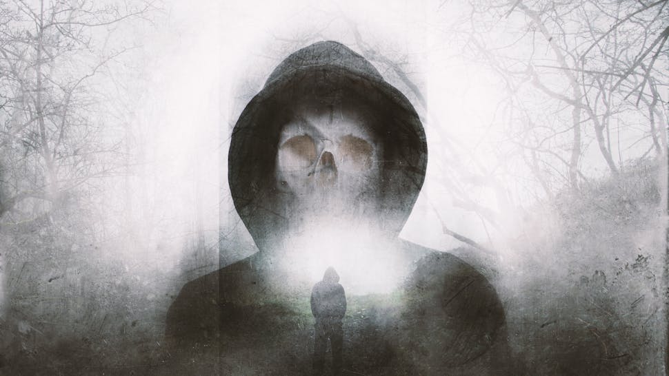 Death A double exposure of a scary hooded figure with a skull for a face. Over layered with a forest in winter. with a blurred, grunge, abstract edit - stock photo