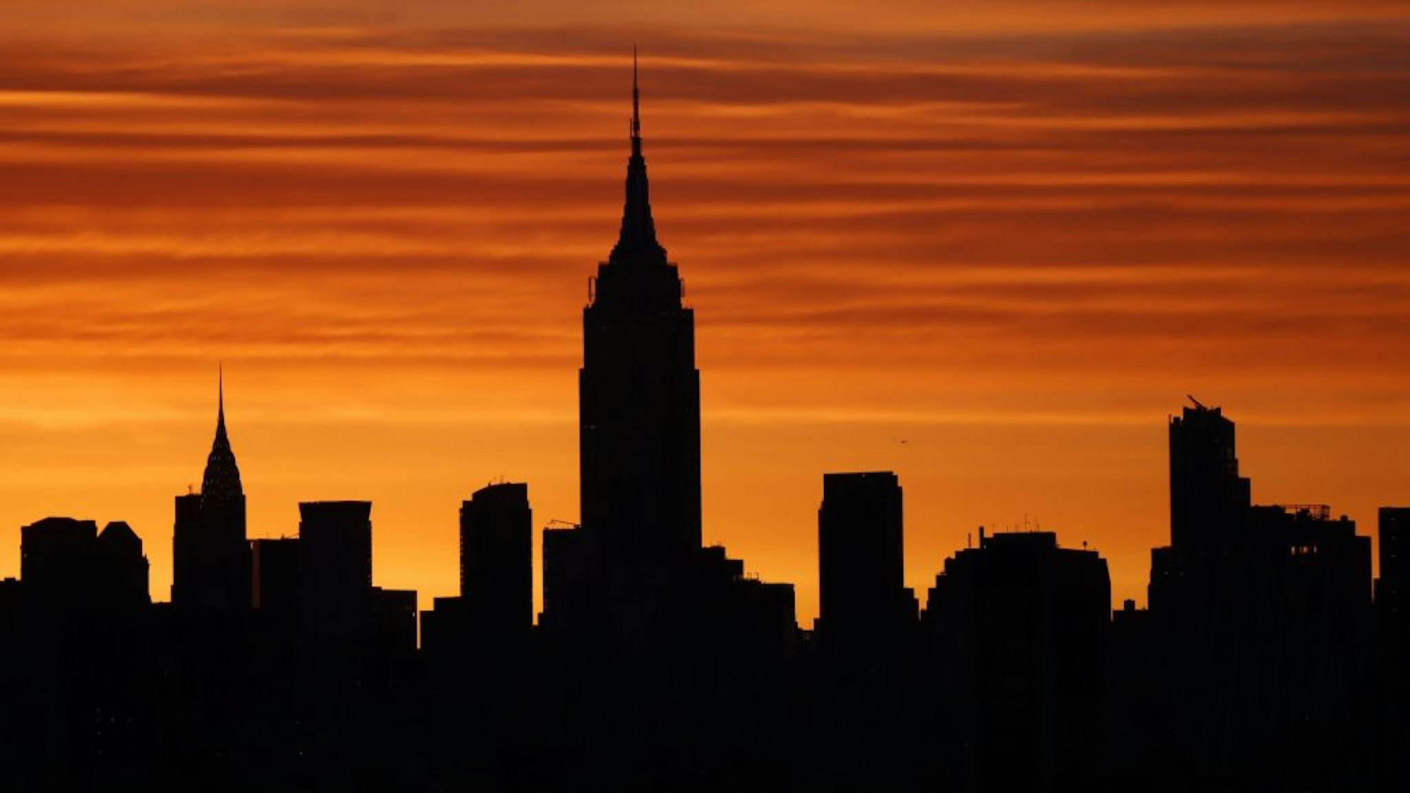 JERSEY CITY, NJ - APRIL 7: The sun rises behind the Empire State Building and Chrysler Building in New York City on April 7, 2021 as seen from Jersey City, New Jersey.