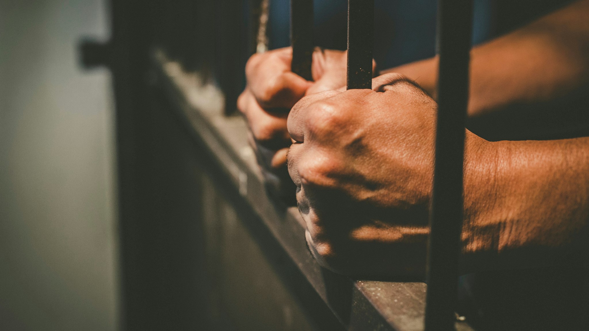Cropped Hands Of Male Prisoner Holding Prison Bars - stock photo