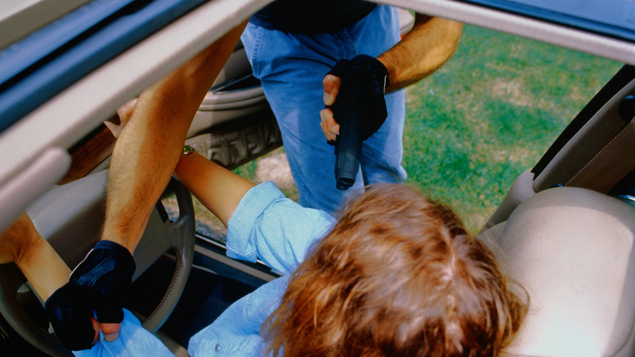 Carjacker forcing woman out of car at gunpoint, view through sun-roof - stock photo