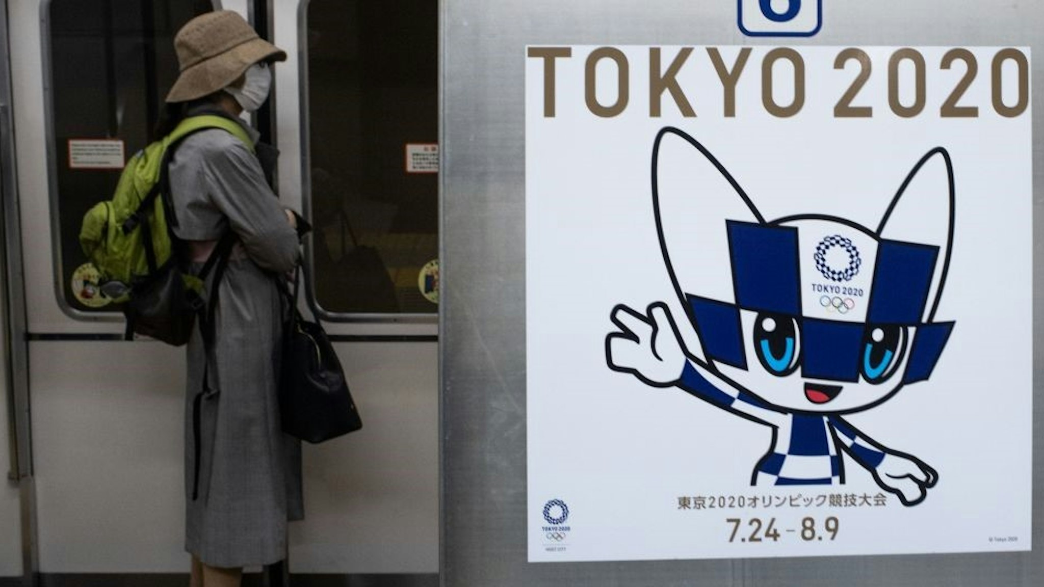 TOPSHOT - A passenger wearing a face mask stands next to a poster of Tokyo 2020 Olympic mascot Miraitowa on a train in Tokyo on April 20, 2020. - A Japanese expert who has criticised the country's response to the coronavirus warned on April 20 that he is "pessimistic" that the postponed Olympics can be held even in 2021. (Photo by Philip FONG / AFP) (Photo by