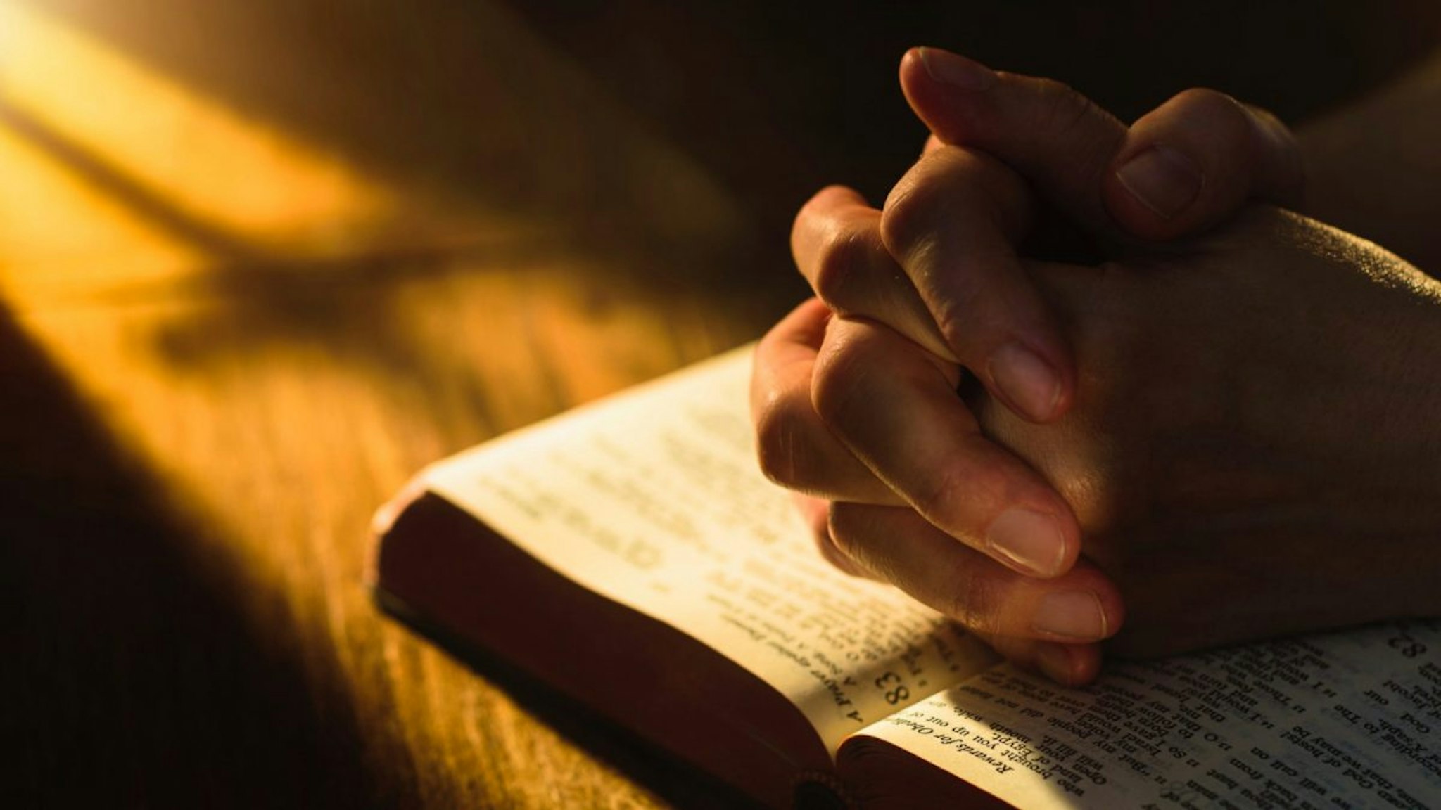 Close up of hands clasped on open Bible - stock photo.