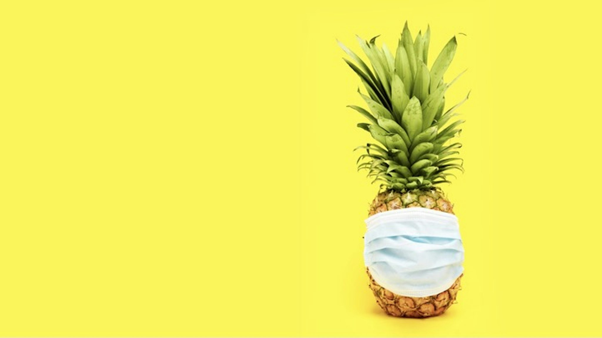 Pineapple with mask on yellow background - stock photo Pineapple with mask on yellow background ENRIQUE MICAELO SANCHEZ via Getty Images