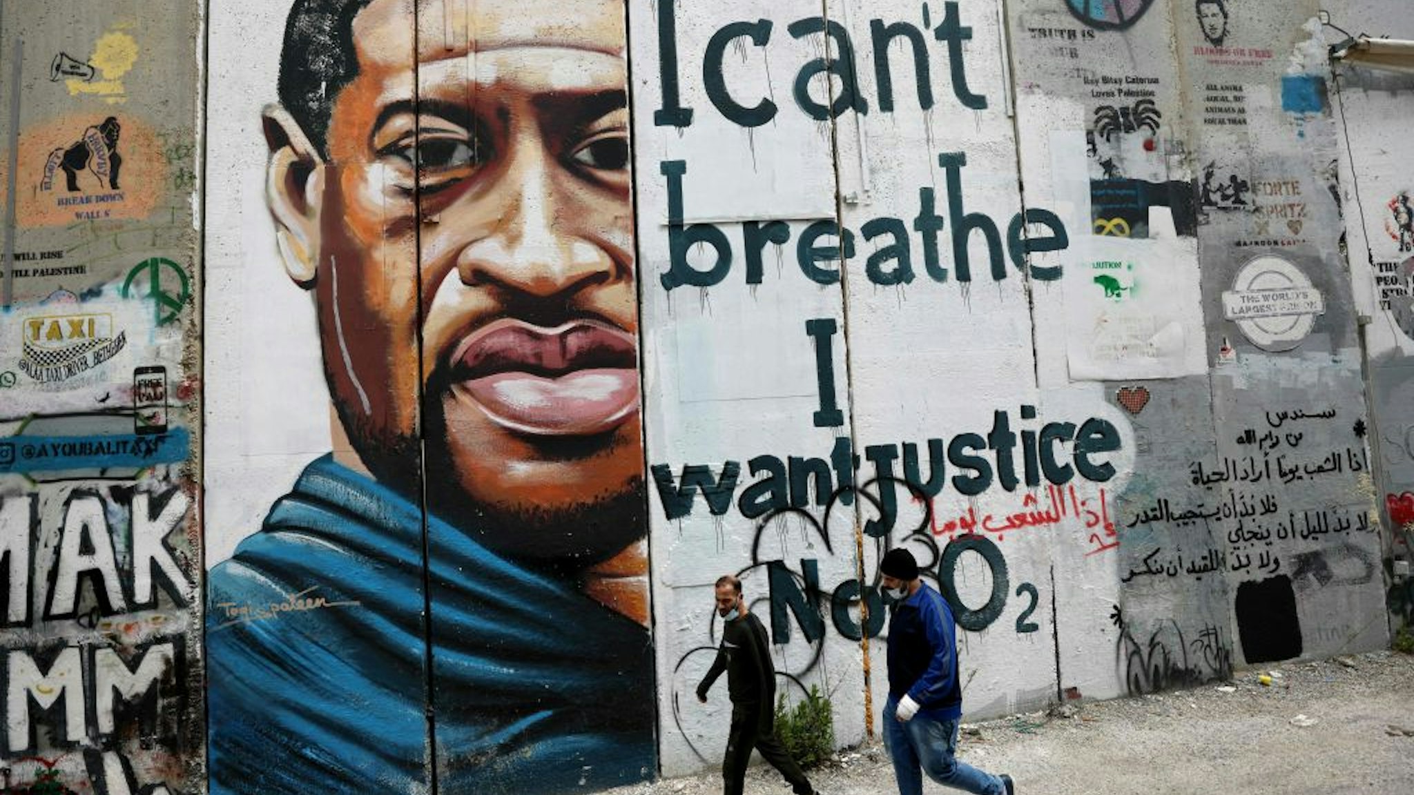 PALESTINIAN-ISRAEL-US-RACISM-POLICE-TRIAL-FLOYD People walk past a mural showing the face of George Floyd, an unarmed handcuffed black man who died after a white policeman knelt on his neck during an arrest in the US, painted on a section of Israel's controversial separation barrier in the city of Bethlehem in the occupied West Bank on March 31, 2021. - The teenager who took the viral video of George Floyd's death said on March 30, at the trial of the white police officer charged with killing the 46-year-old Black man that she knew at the time "it wasn't right." Darnella Frazier, 18, was among the witnesses who gave emotional testimony on Tuesday at the high-profile trial of former Minneapolis police officer Derek Chauvin. Chauvin, 45, is charged with murder and manslaughter for his role in Floyd's May 25, 2020 death, which was captured on video by Frazier and seen by millions, sparking anti-racism protests around the globe. (Photo by Emmanuel DUNAND / AFP) (Photo by EMMANUEL DUNAND/AFP via Getty Images) EMMANUEL DUNAND / Contributor via Getty Images