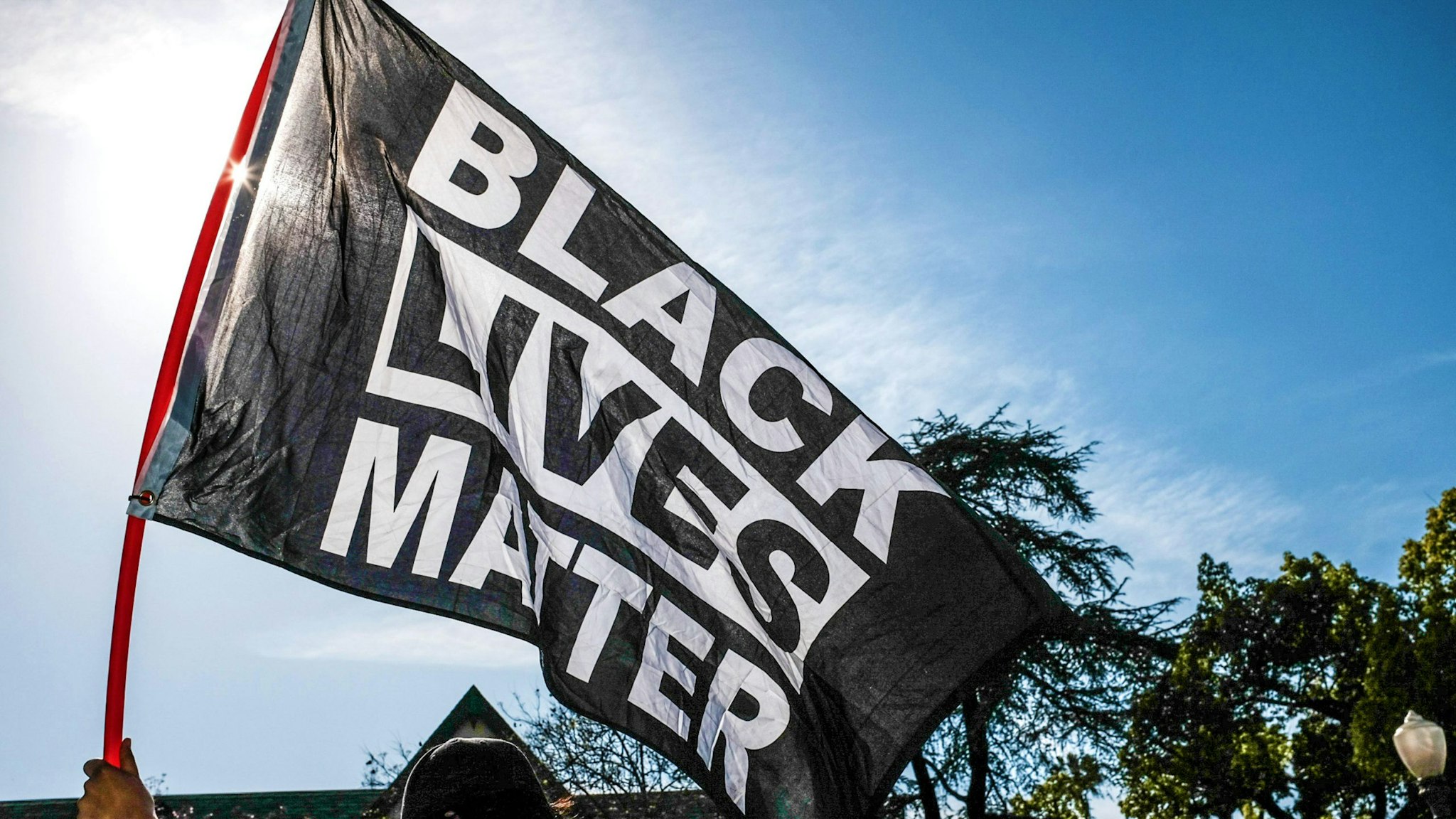 LOS ANGELES, CALIFORNIA, UNITED STATES - 2021/04/20: A protester waves a Black Lives Matter flag during the demonstration. Hours after the verdict of the Derek Chauvin trial, protesters meet outside of Los Angeles Mayor Eric Garcetti's home to protest his proposed funding of the Los Angeles Police Department.