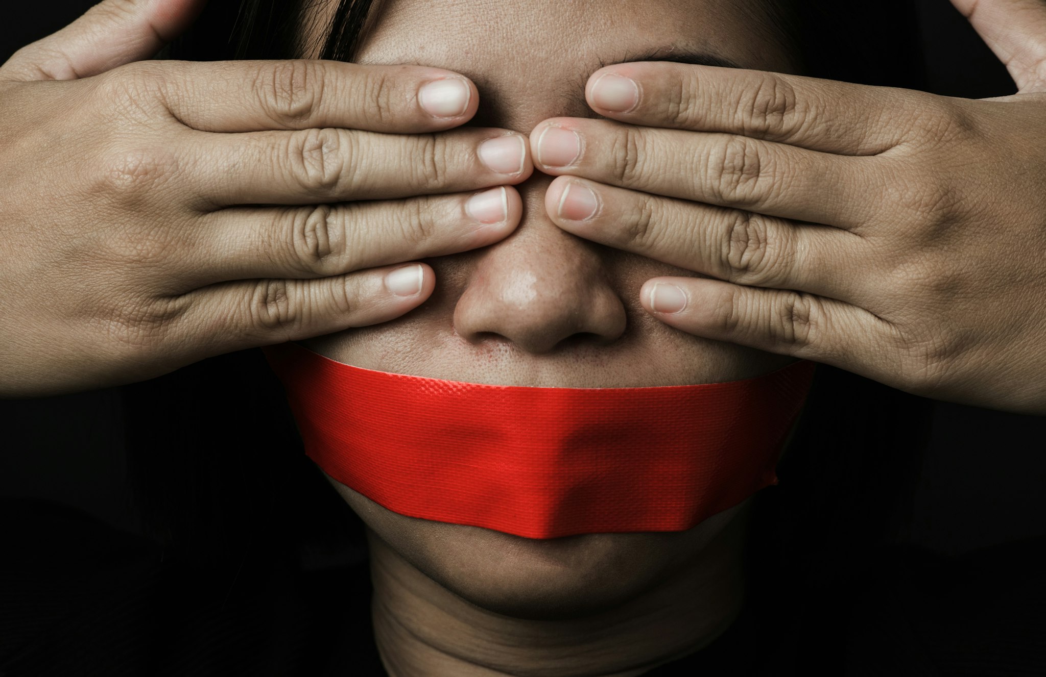 Asian woman blindfold wrapping mouth with red adhesive tape on black background. Freedom speech censorship and stop talk, International Human Right day (Asian woman blindfold wrapping mouth with red adhesive tape on black background. Freedom speech ce