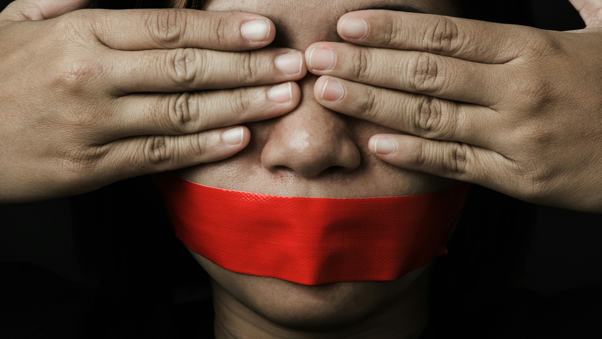 Asian woman blindfold wrapping mouth with red adhesive tape on black background. Freedom speech censorship and stop talk, International Human Right day (Asian woman blindfold wrapping mouth with red adhesive tape on black background. Freedom speech ce