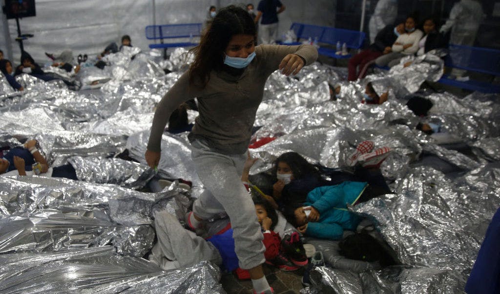 TOPSHOT - A young female minor walks over others as they lie inside a pod for females at the Donna Department of Homeland Security holding facility, the main detention center for unaccompanied children in the Rio Grande Valley run by the US Customs and Border Protection, (CBP), in Donna, Texas on March 30, 2021. - The minors are housed by the hundreds in eight pods that are about 3,200 square feet in size. Many of the pods had more than 500 children in them. The Biden administration on Tuesday for the first time allowed journalists inside its main detention facility at the border for migrant children, revealing a severely overcrowded tent structure where more than 4,000 kids and families were crammed into pods and the youngest kept in a large play pen with mats on the floor for sleeping. (Photo by Dario Lopez-Mills / POOL / AFP) (Photo by DARIO LOPEZ-MILLS/POOL/AFP via Getty Images)