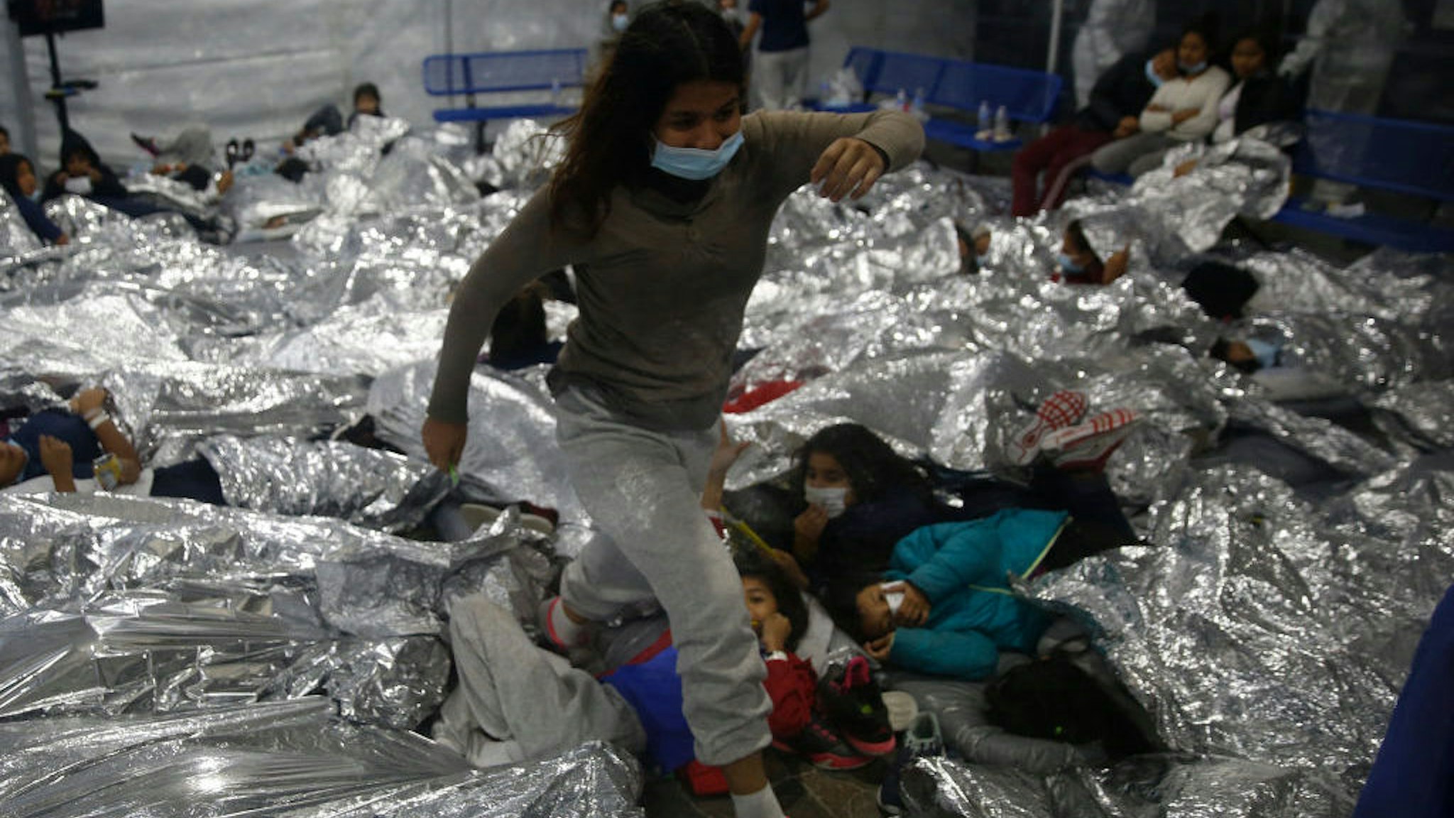 TOPSHOT - A young female minor walks over others as they lie inside a pod for females at the Donna Department of Homeland Security holding facility, the main detention center for unaccompanied children in the Rio Grande Valley run by the US Customs and Border Protection, (CBP), in Donna, Texas on March 30, 2021. - The minors are housed by the hundreds in eight pods that are about 3,200 square feet in size. Many of the pods had more than 500 children in them. The Biden administration on Tuesday for the first time allowed journalists inside its main detention facility at the border for migrant children, revealing a severely overcrowded tent structure where more than 4,000 kids and families were crammed into pods and the youngest kept in a large play pen with mats on the floor for sleeping. (Photo by Dario Lopez-Mills / POOL / AFP) (Photo by DARIO LOPEZ-MILLS/POOL/AFP via Getty Images)