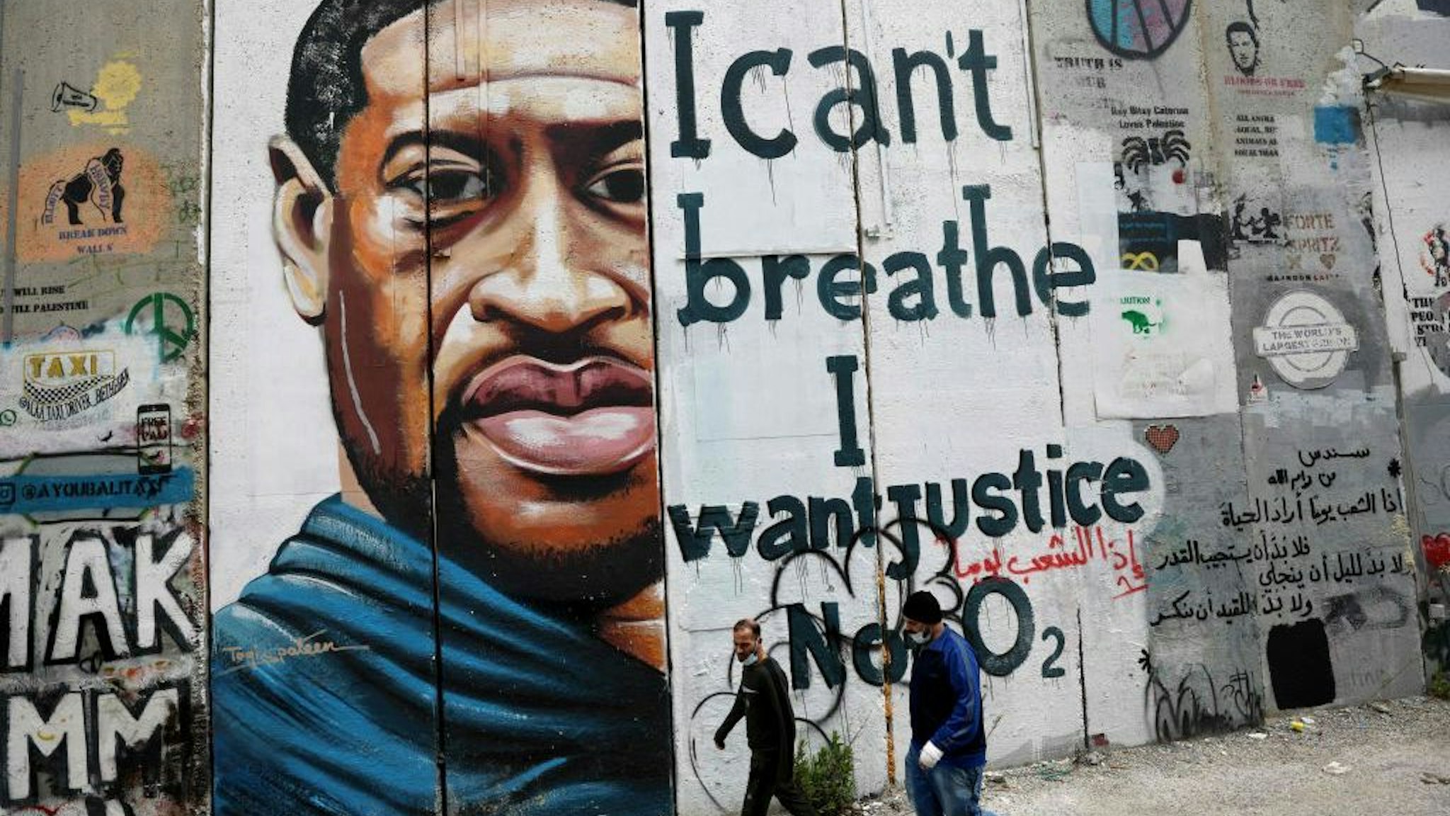 People walk past a mural showing the face of George Floyd, an unarmed handcuffed black man who died after a white policeman knelt on his neck during an arrest in the US, painted on a section of Israel's controversial separation barrier in the city of Bethlehem in the occupied West Bank on March 31, 2021. (Photo by Emmanuel DUNAND / AFP) (Photo by EMMANUEL DUNAND/AFP via Getty Images)