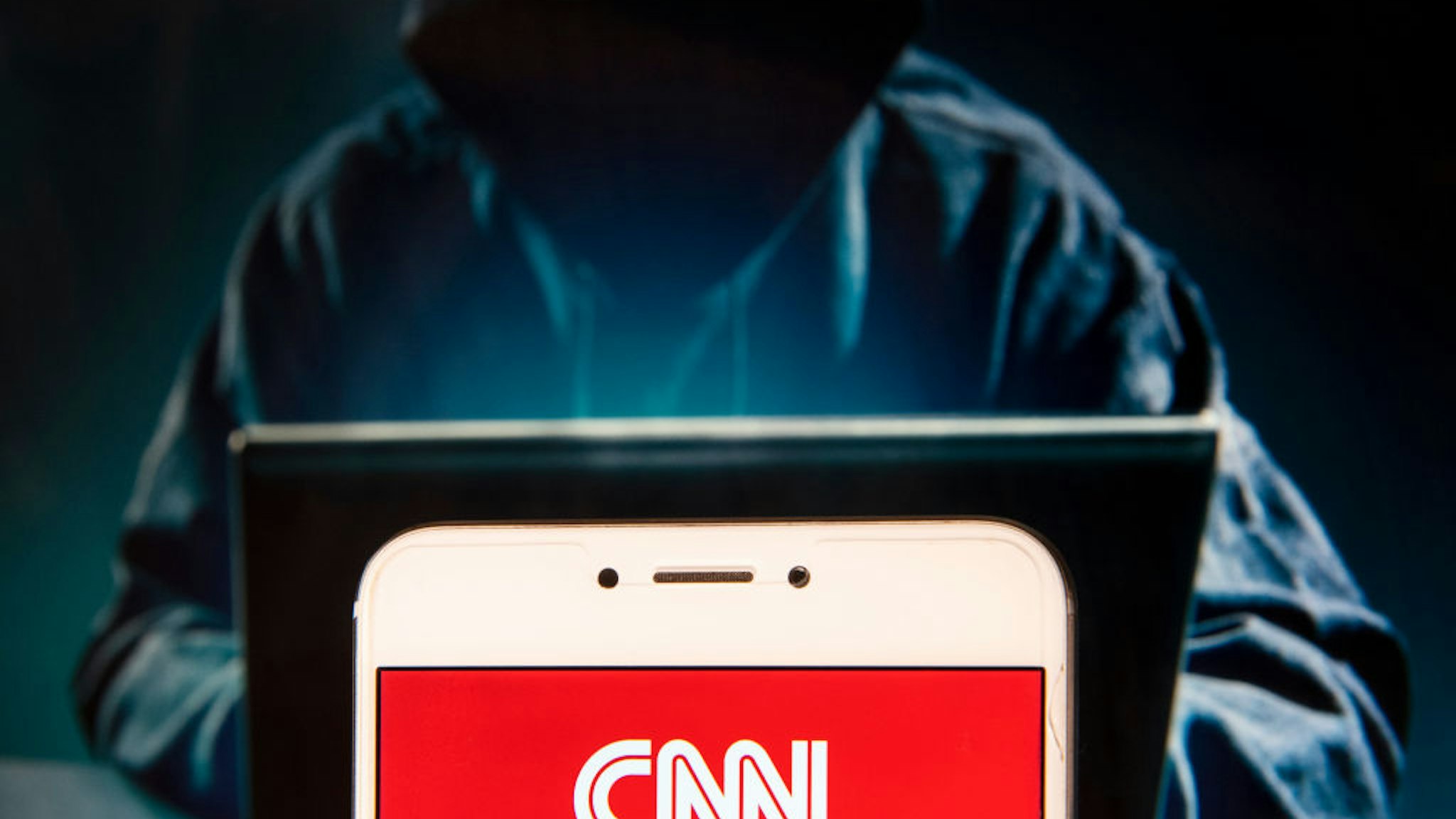 In this photo illustration, the CNN logo is seen displayed on an Android mobile device with a figure of hacker in the background.