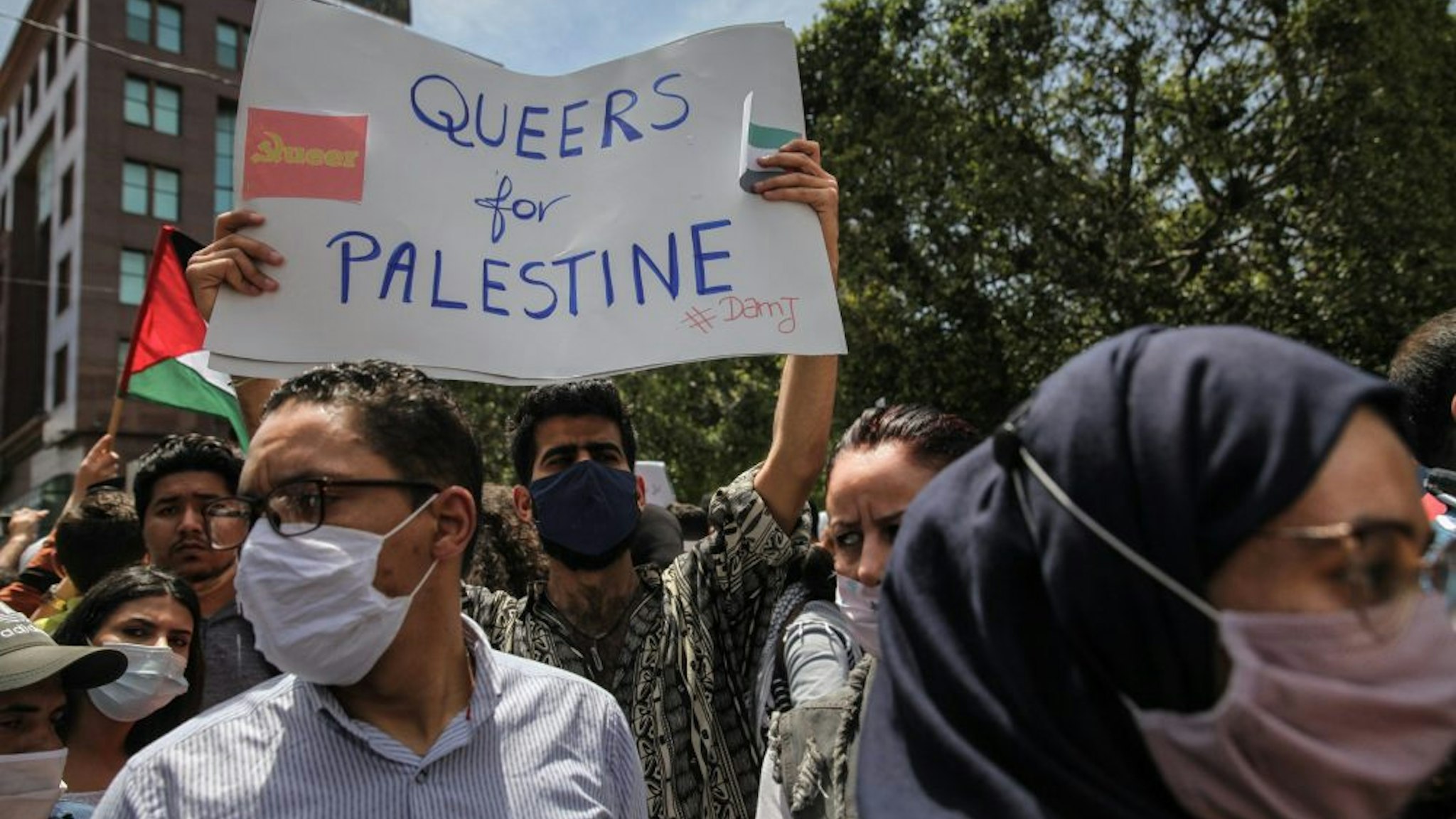 A protester lifts a placard that reads in english, Queers for Palestine as an other protester waves the Palestinian flag during a demonstration held by thousands of Tunisian an Palestinian demonstrators on avenue Habib Bourguiba in the capital Tunis, Tunisia, on May 15, 2021, in support with the Palestinian people and to protest against the Israel's air strikes on Gaza strip and against the Israeli violations in the occupied territories in Palestine, especially in the Palestinian neighborhood in East Jerusalem, Sheikh Jarrah.