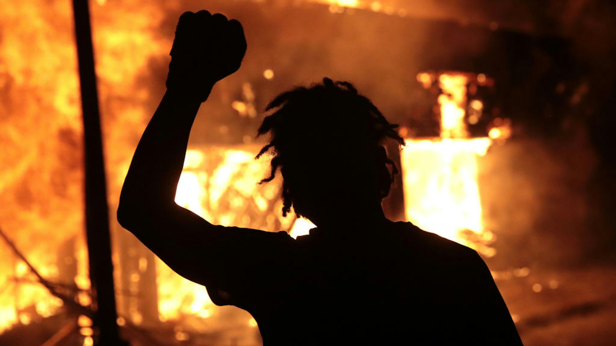 MINNEAPOLIS, MINNESOTA - MAY 29: A man raises his fist in front of a burning building during protests sparked by the death of George Floyd while in police custody on May 29, 2020 in Minneapolis, Minnesota. Earlier today, former Minneapolis police officer Derek Chauvin was taken into custody for Floyd's death. Chauvin has been accused of kneeling on Floyd's neck as he pleaded with him about not being able to breathe. Floyd was pronounced dead a short while later. Chauvin and 3 other officers, who were involved in the arrest, were fired from the police department after a video of the arrest was circulated. (Photo by Scott Olson/Getty Images)
