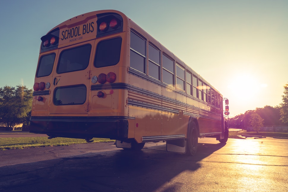 Low angle view of yellow school buss from right rear at dusk looking into setting sun